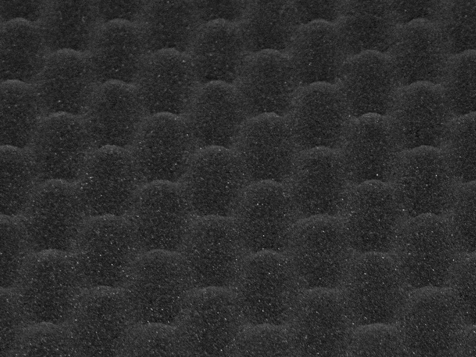 Close-up of dark gray egg crate foam with rounded, textured peaks and valleys for sound absorption or cushioning.