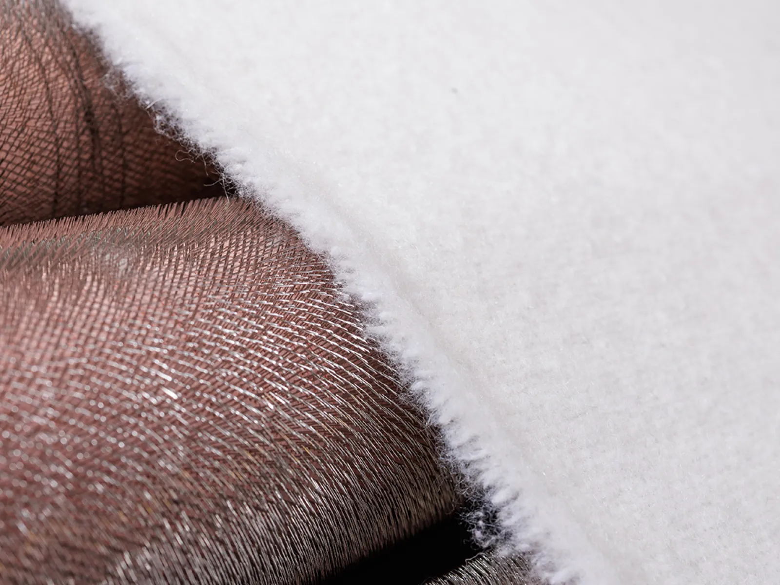 Close-up of a white fabric edge over metallic copper-colored woven material showing texture contrast.