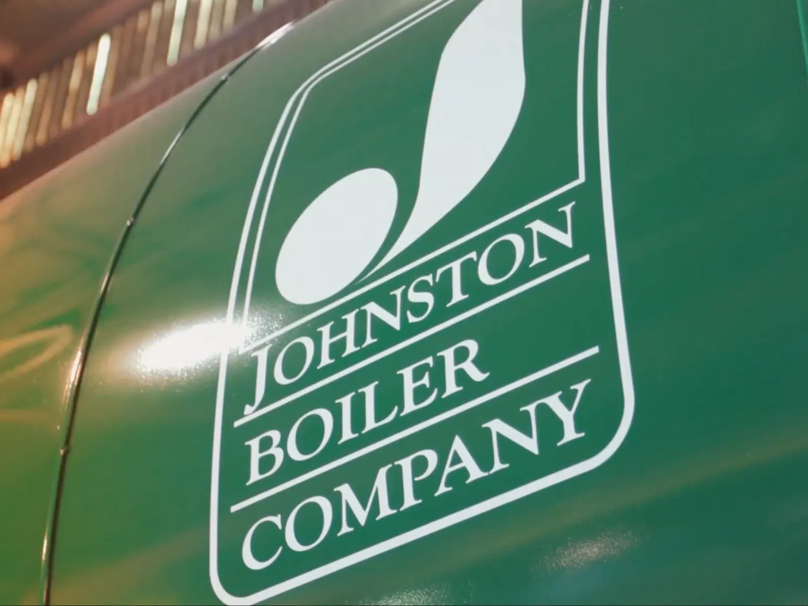 Johnston Boiler Company logo displayed on a green boiler surface with curved lines and light reflection.
