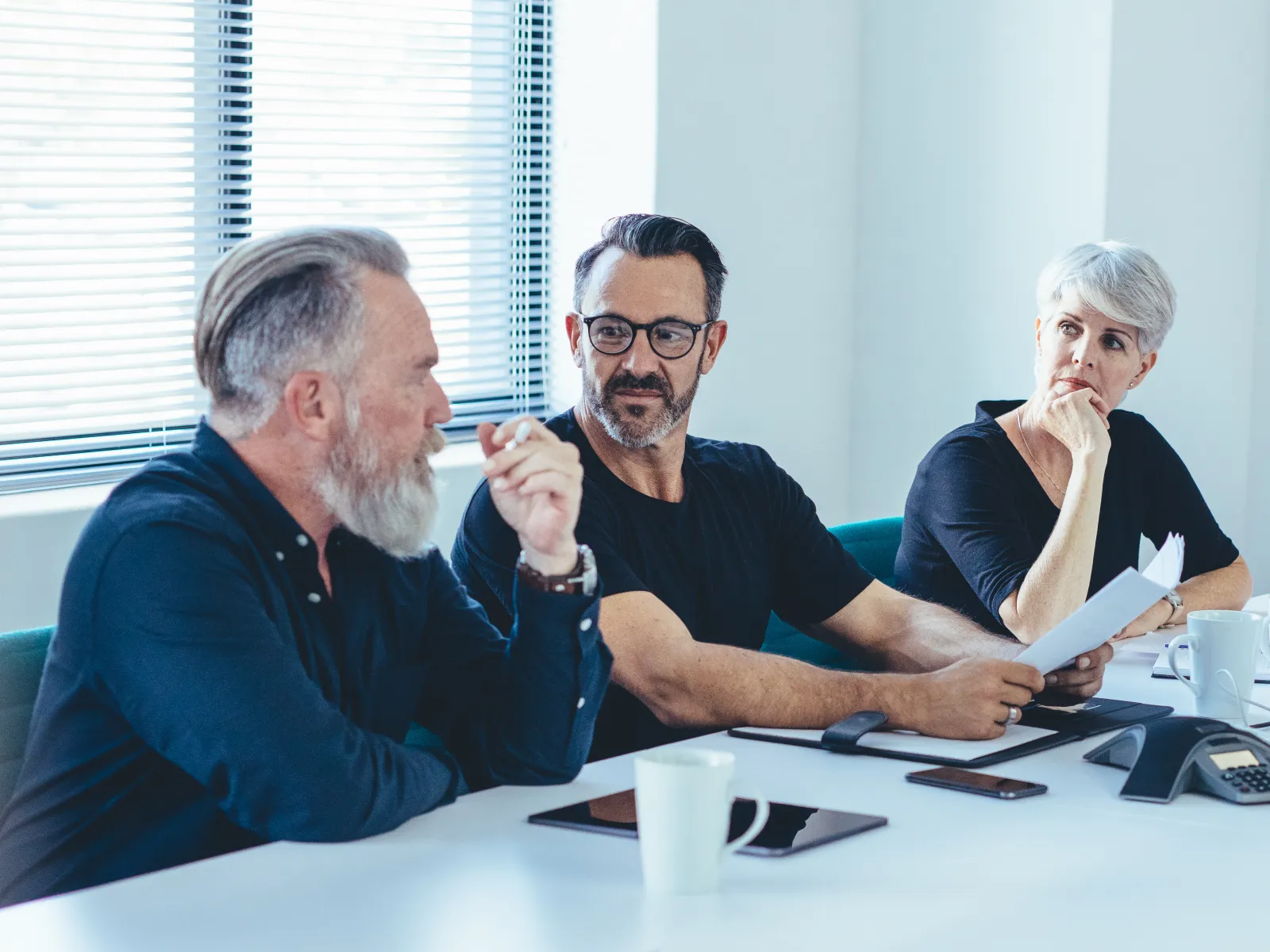 Five diverse professionals engaged in a focused meeting around a white conference table with laptops and documents.