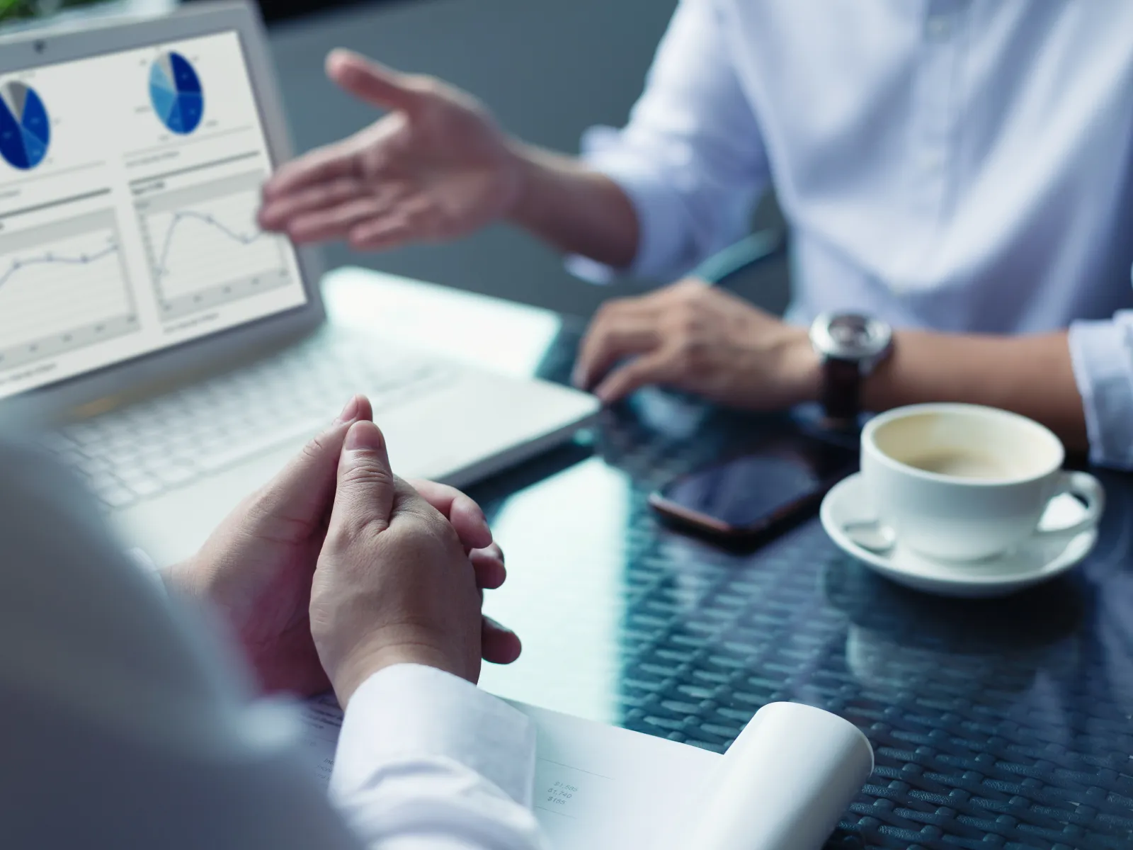 Two business professionals discussing data charts on a laptop with coffee and smartphone on the table