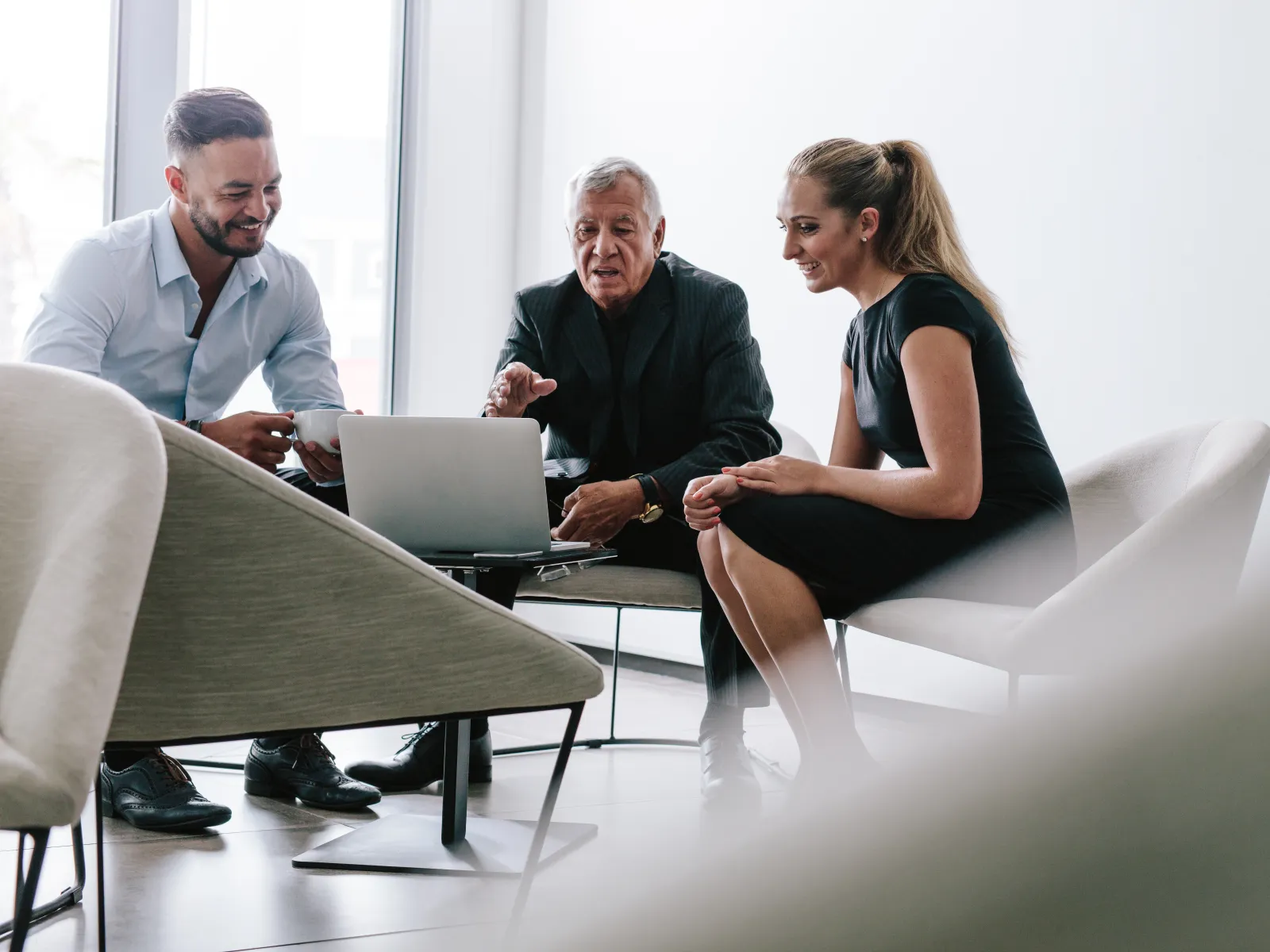 Three diverse business professionals collaborating over a laptop in a bright modern office lounge area