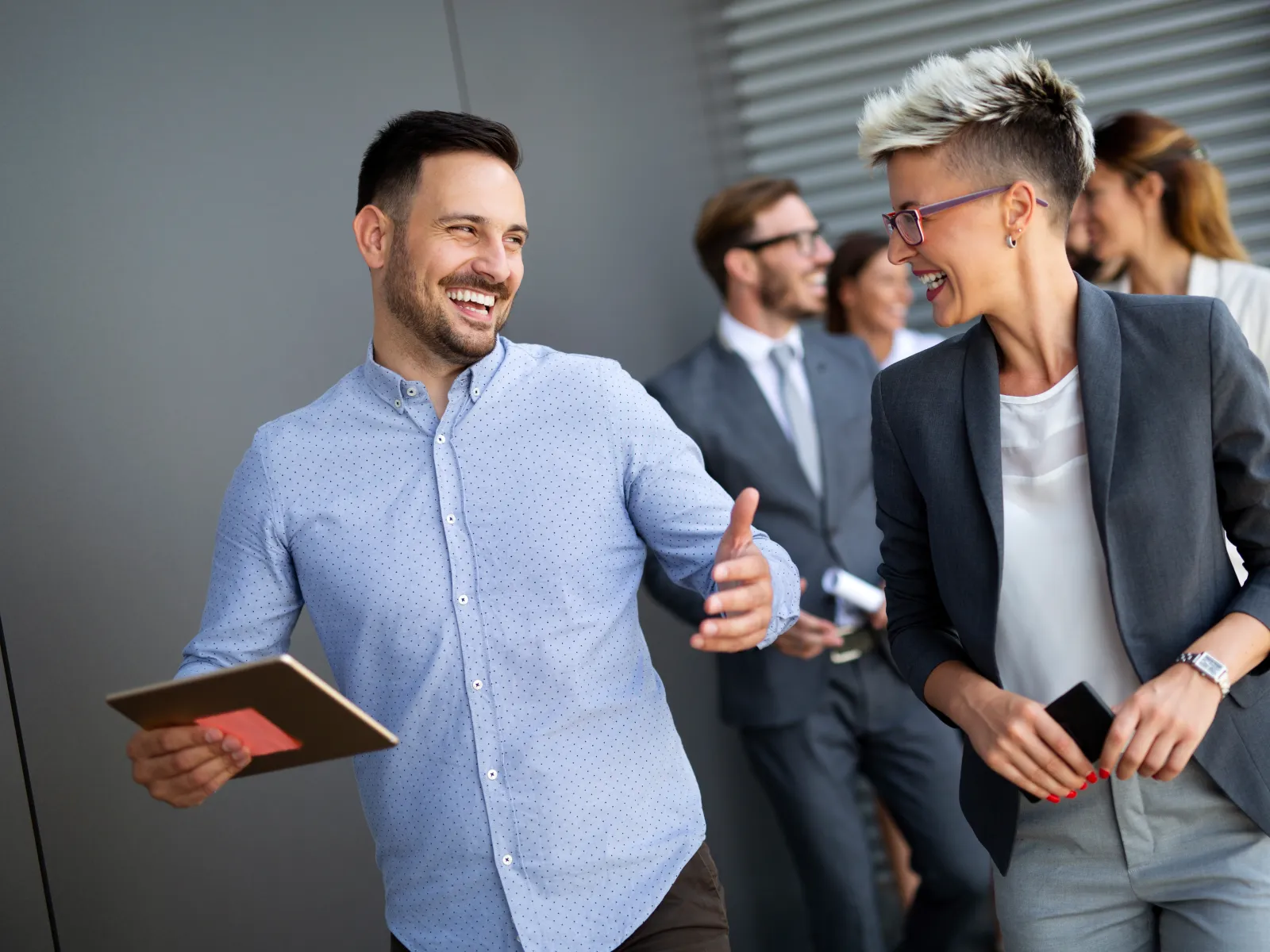 Two business colleagues smiling and talking while walking with a group of professionals in the background.