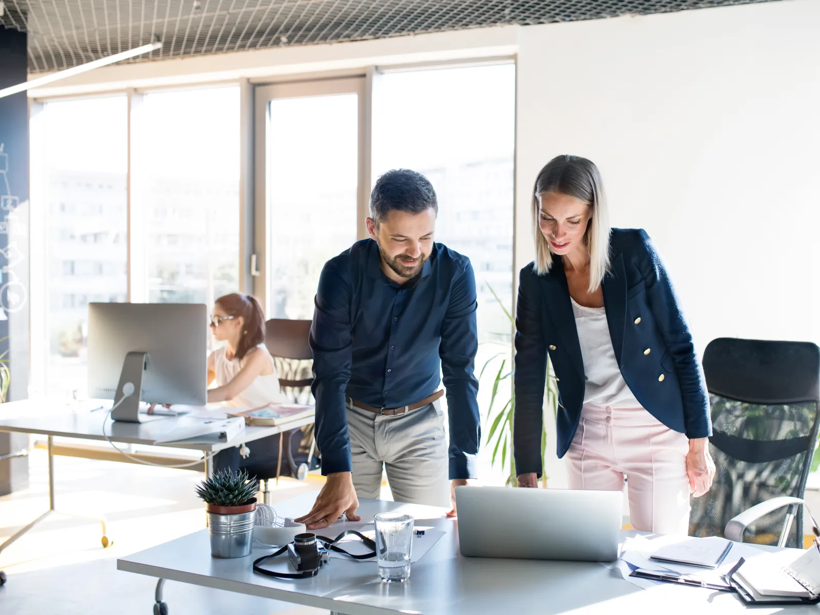 Two professionals collaborating on a project while looking at a laptop in a bright modern office.