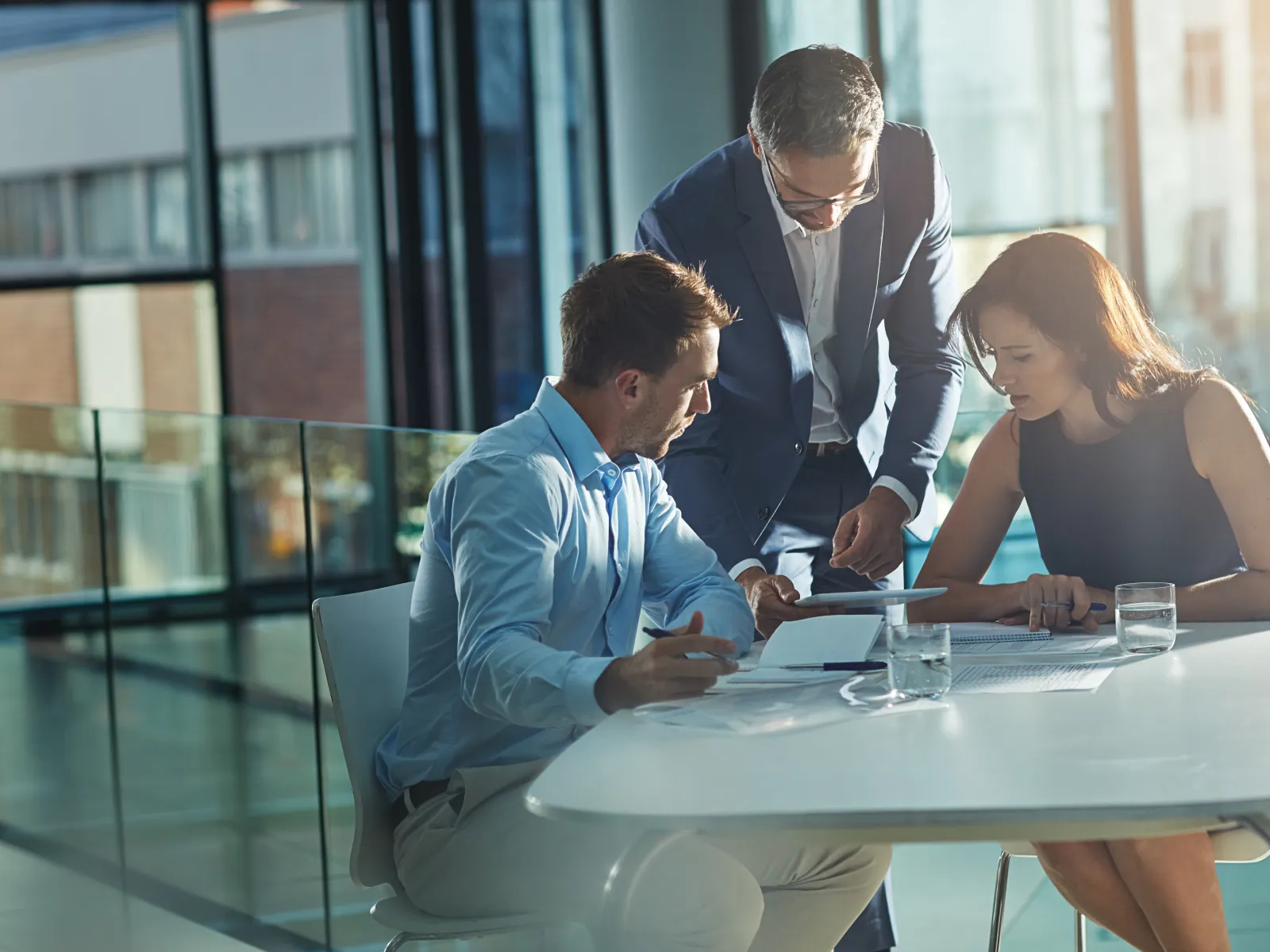 Three business professionals discussing documents together in a modern office meeting room with natural light
