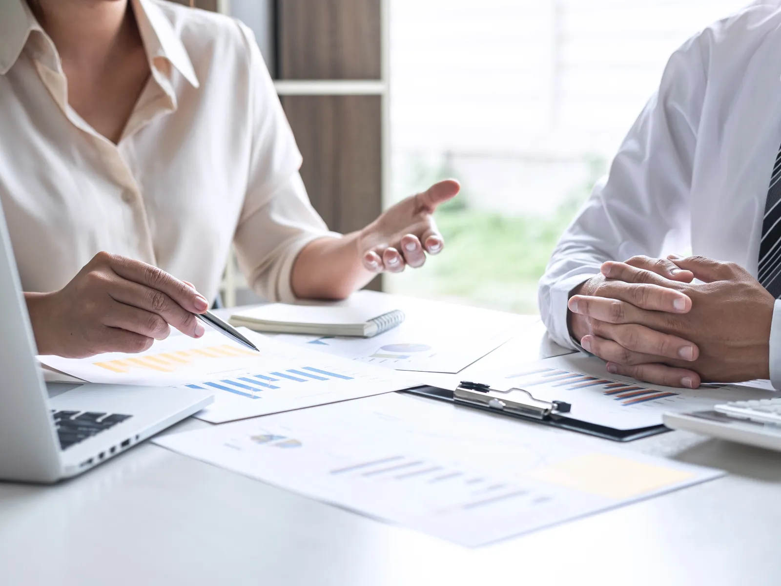Two professionals discussing financial charts and data during a business meeting at a bright office desk.