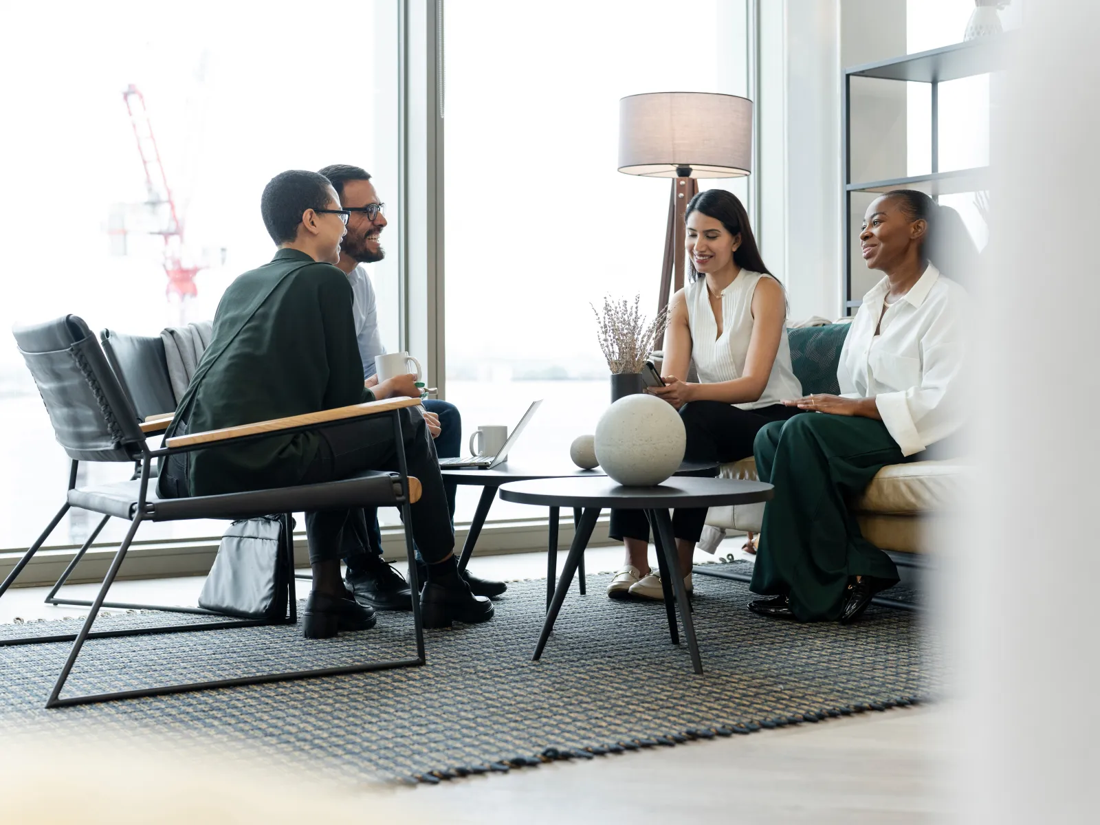 Four diverse professionals having a casual meeting in a modern office lounge with large windows and natural light