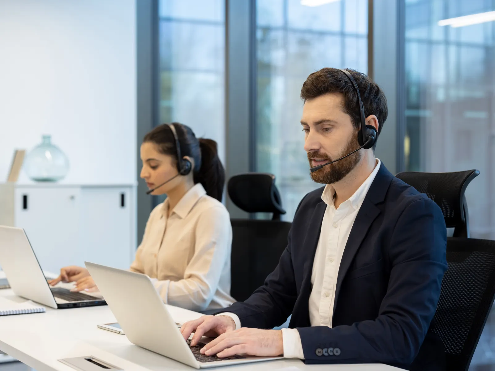 Customer service representatives wearing headsets working on laptops in modern office environment