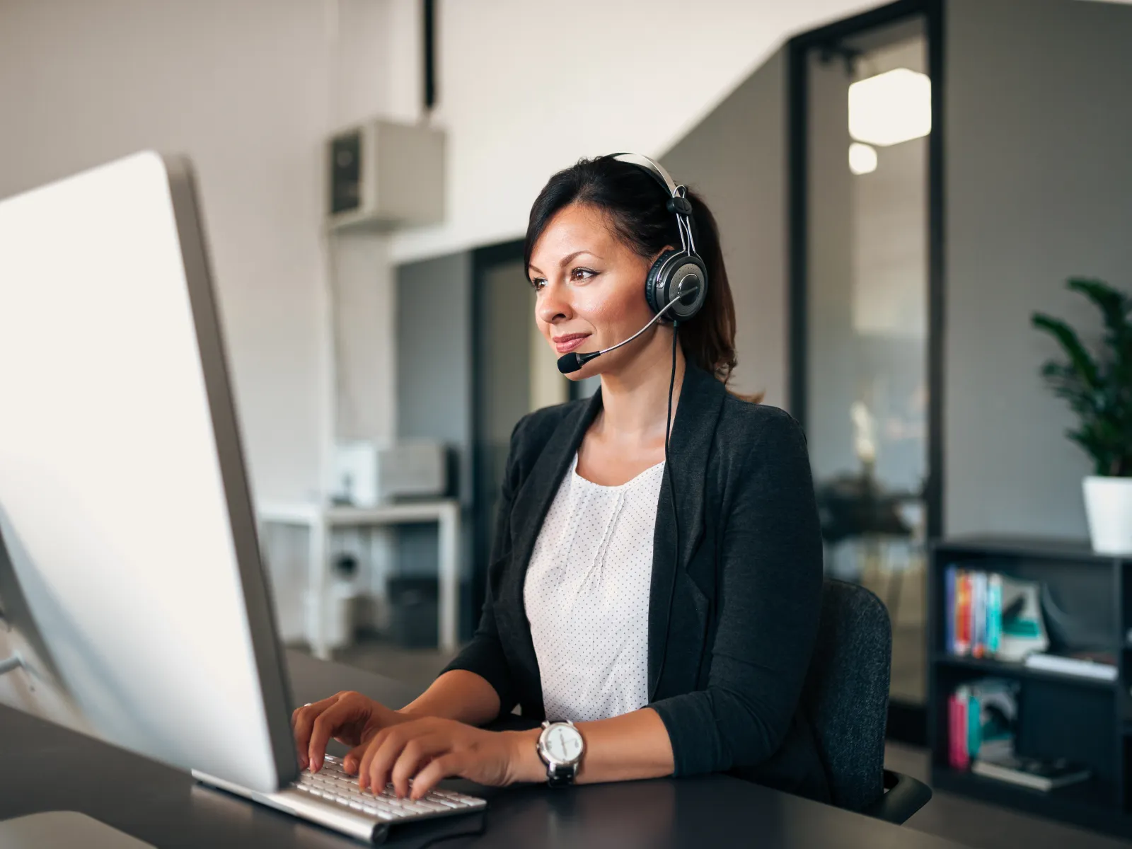 Customer service representative wearing headset working on computer in modern office environment