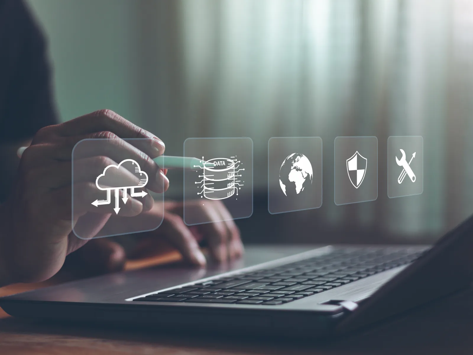 Hand interacting with digital icons representing cloud computing, data, global network, security, and tools over laptop keyboard.