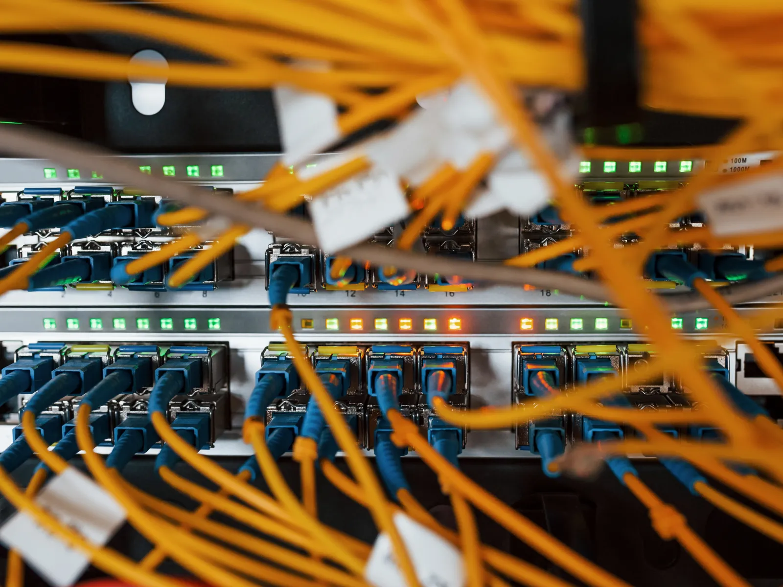 Close-up of network server with numerous blue Ethernet and yellow fiber optic cables connected and green indicator lights.