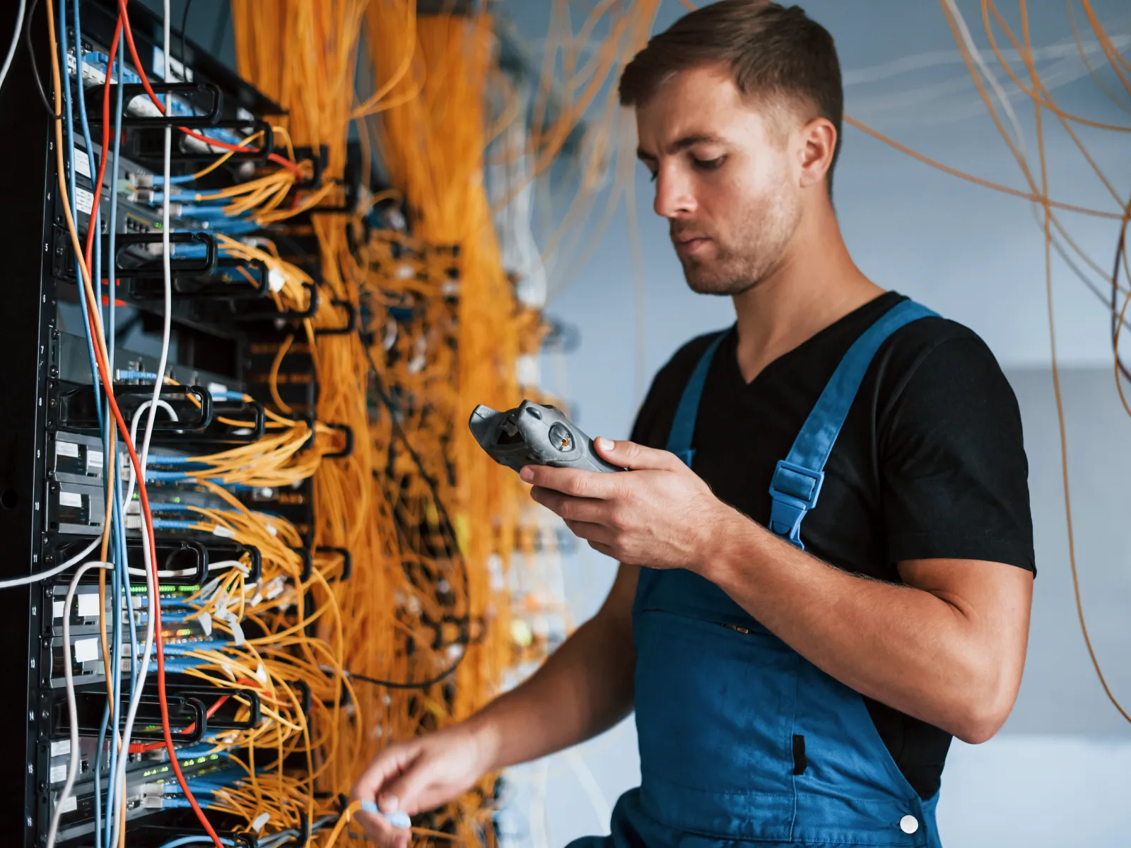 Technician in blue overalls working with network cables and server equipment in a data center room.