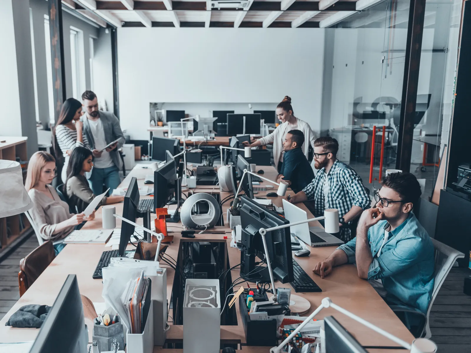Modern office with team members collaborating and working at desks with computers in an open workspace.