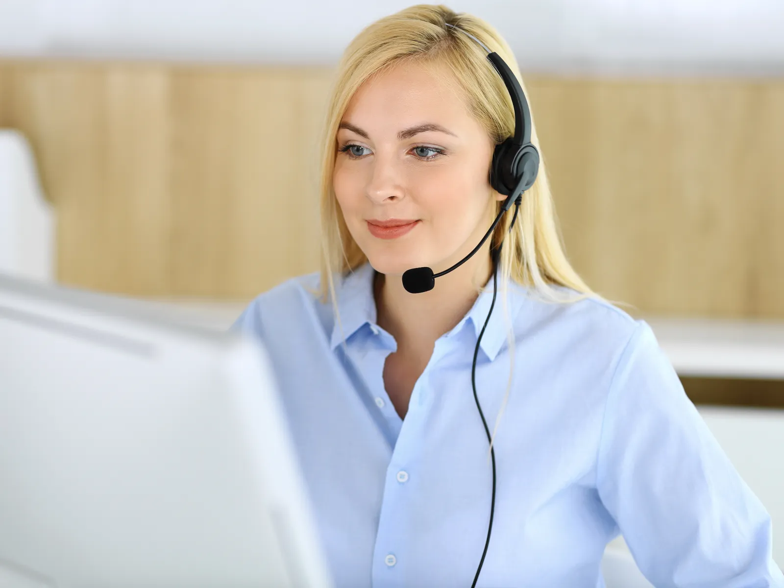 Smiling customer service representative wearing headset working on computer in modern office environment