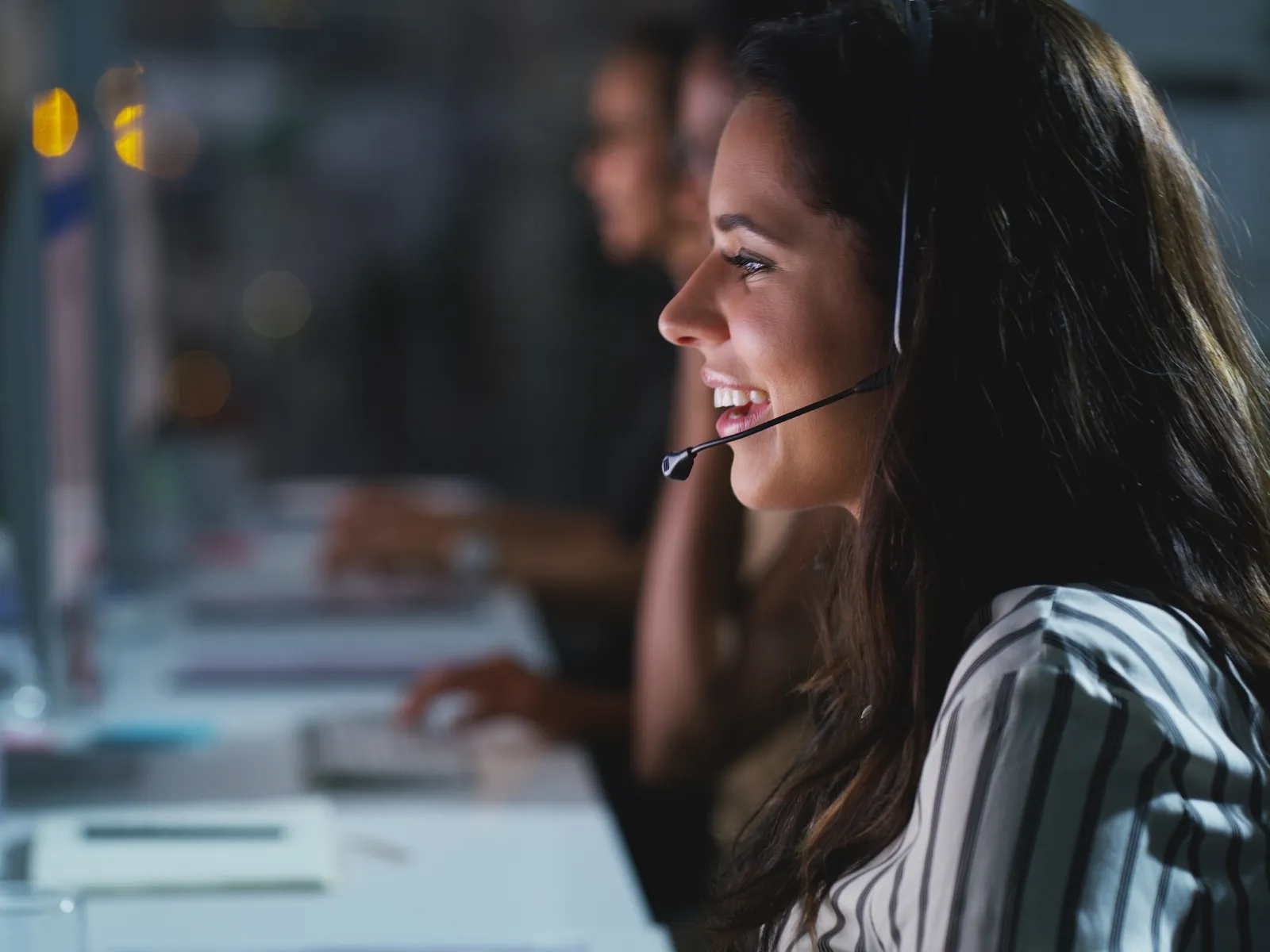 Customer support representative wearing headset working on computer in a modern office at night.