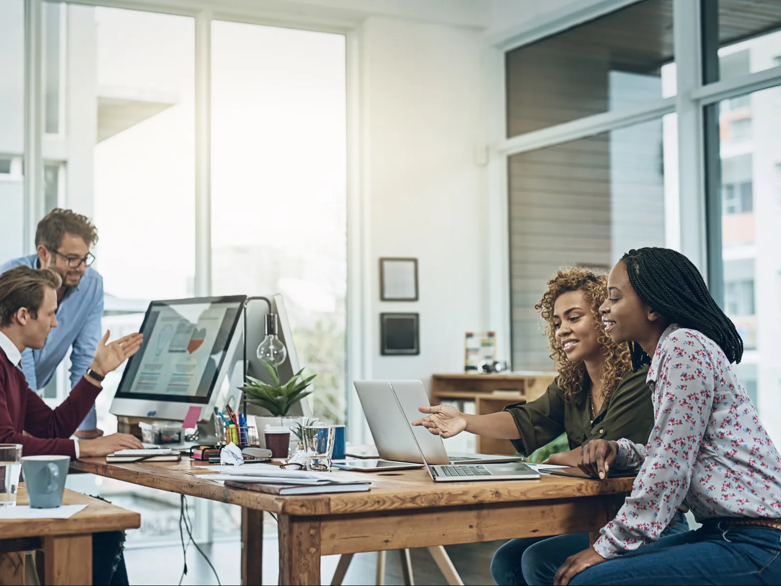 Diverse team collaborating in modern office with laptops and desktop computers during a business meeting.
