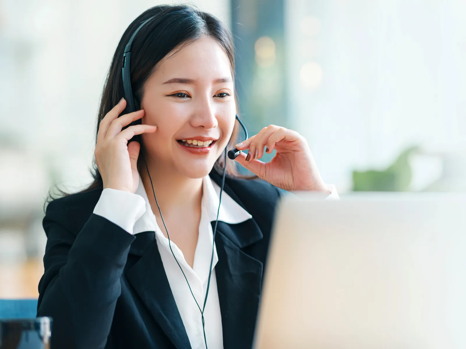 Smiling customer service agent wearing headset working on laptop in bright office environment