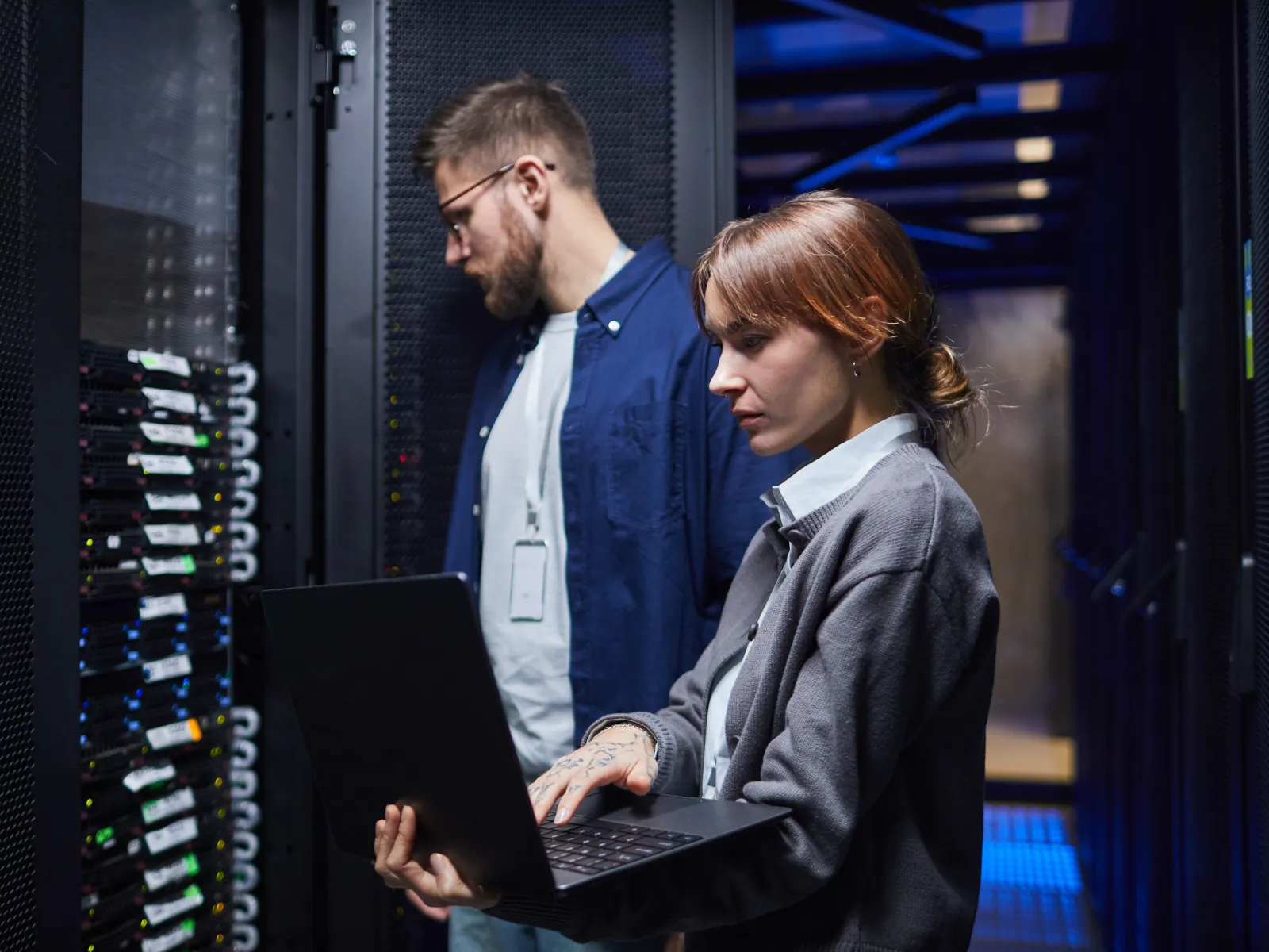 IT professionals working on servers in a data center, managing network and computer systems with laptops and equipment.