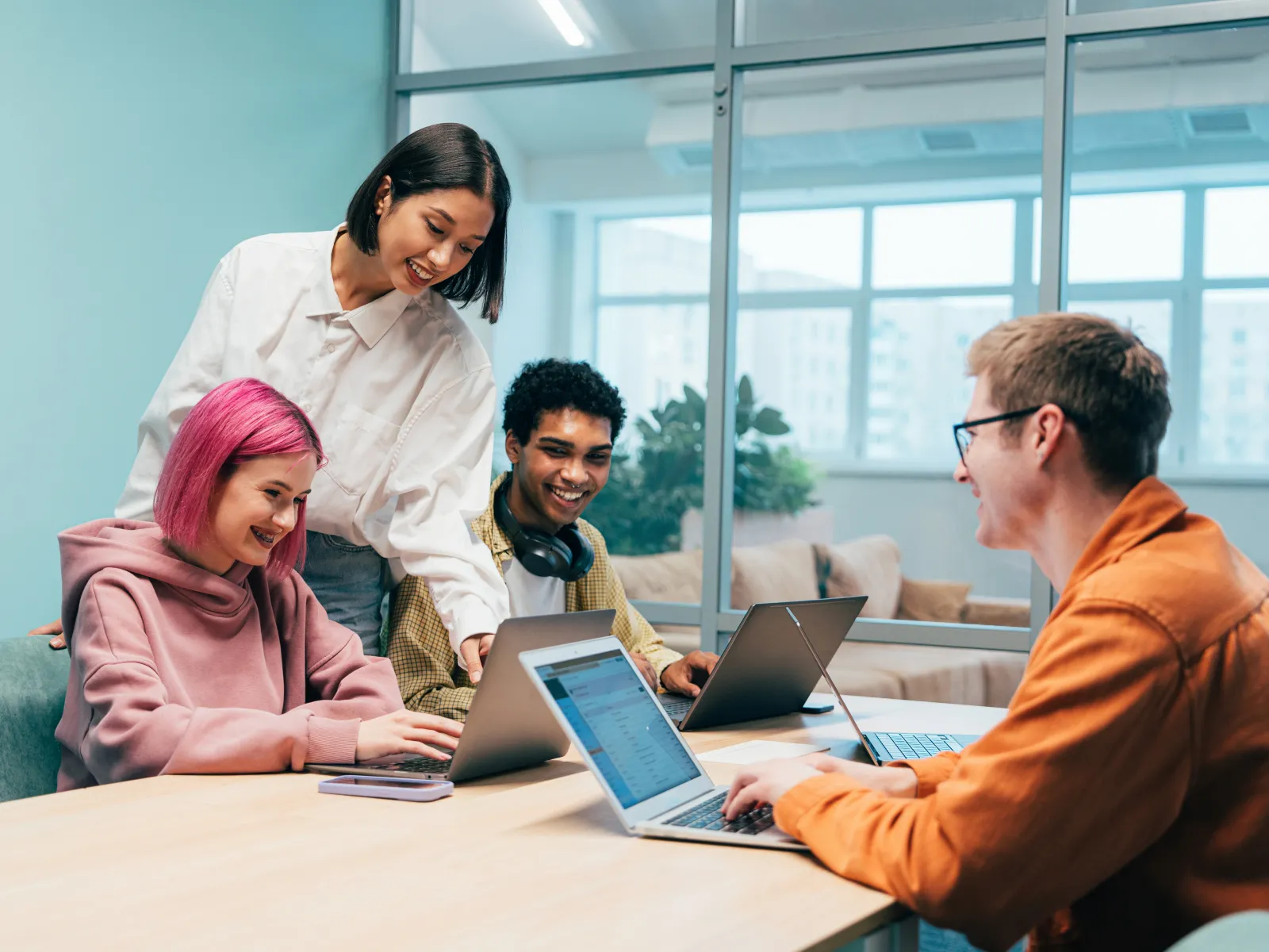 Young diverse coworkers collaborating on laptops in a bright modern office meeting room.