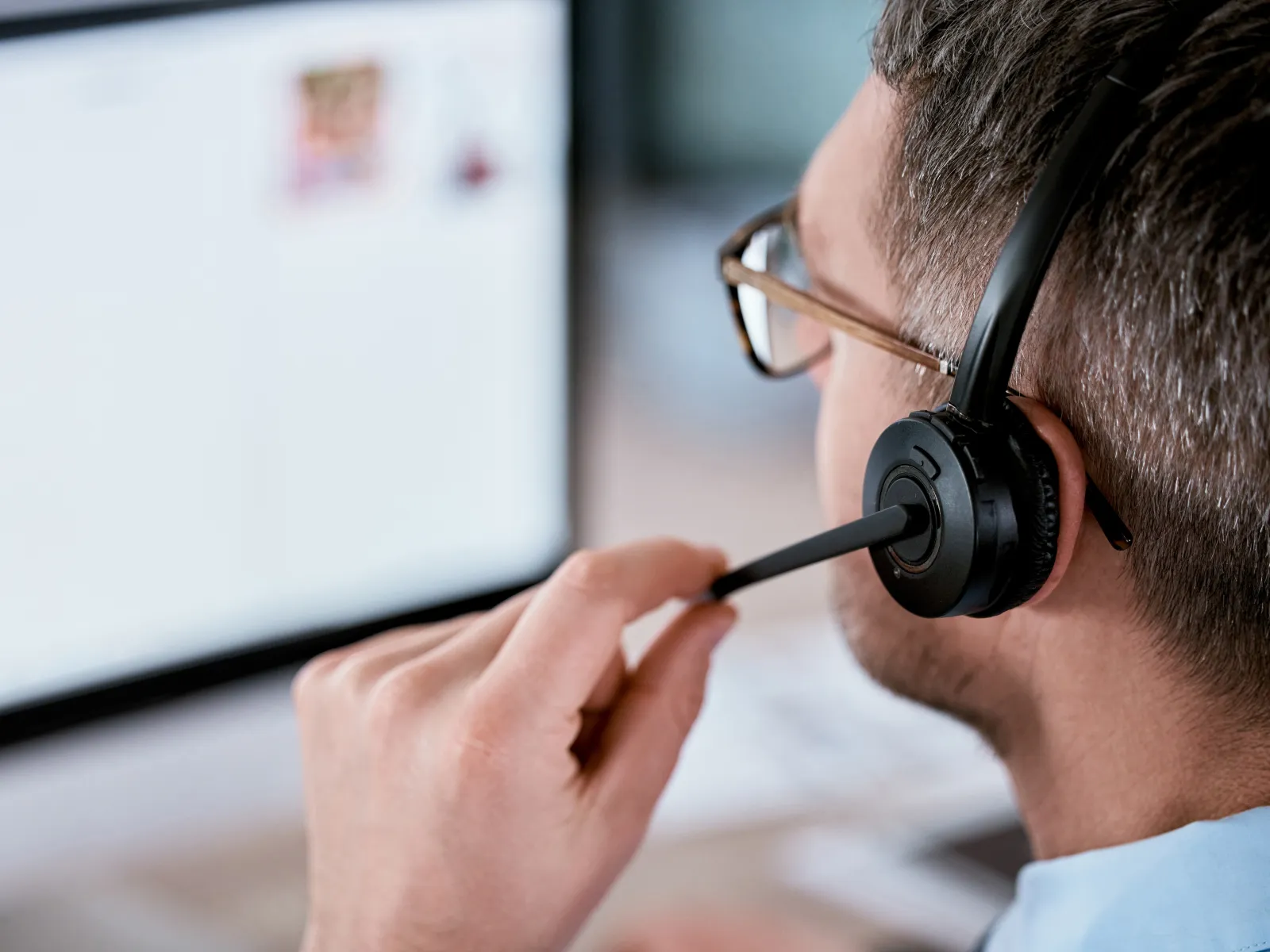 Customer service representative wearing headset working on computer with blurred screen in background