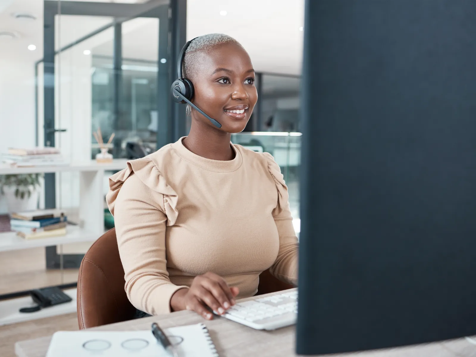 Smiling woman wearing headset working at computer in modern office environment providing customer support.