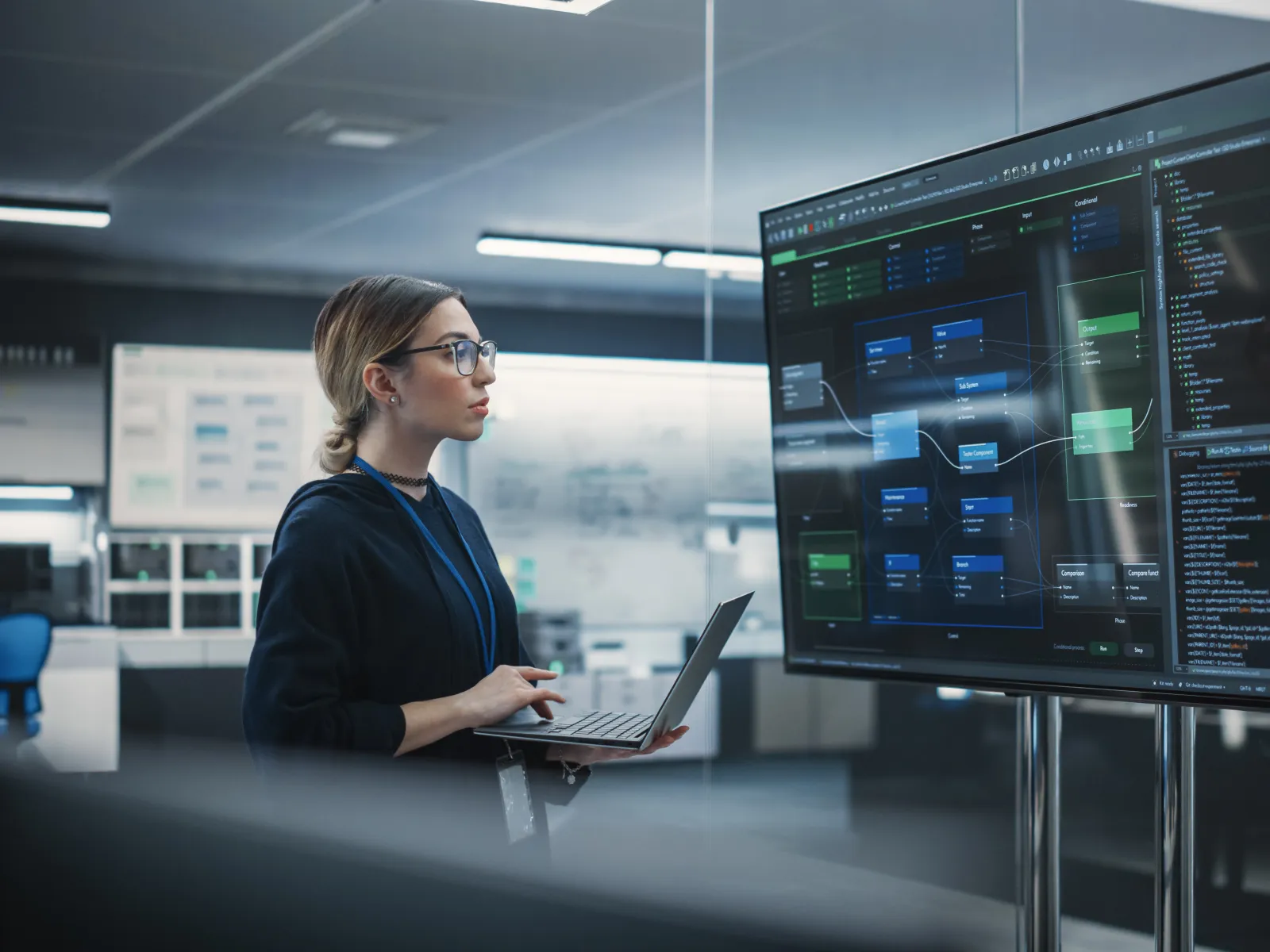 Female software engineer reviewing complex code flowcharts on a large monitor in a modern office environment