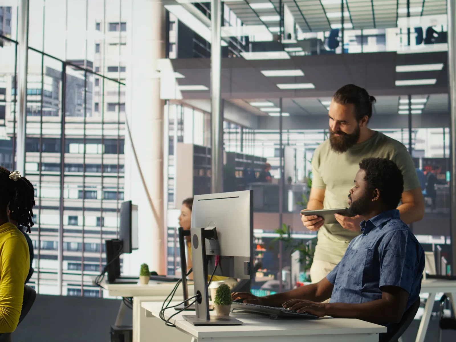 Colleagues collaborating in a modern office with large windows and computer workstations during the day