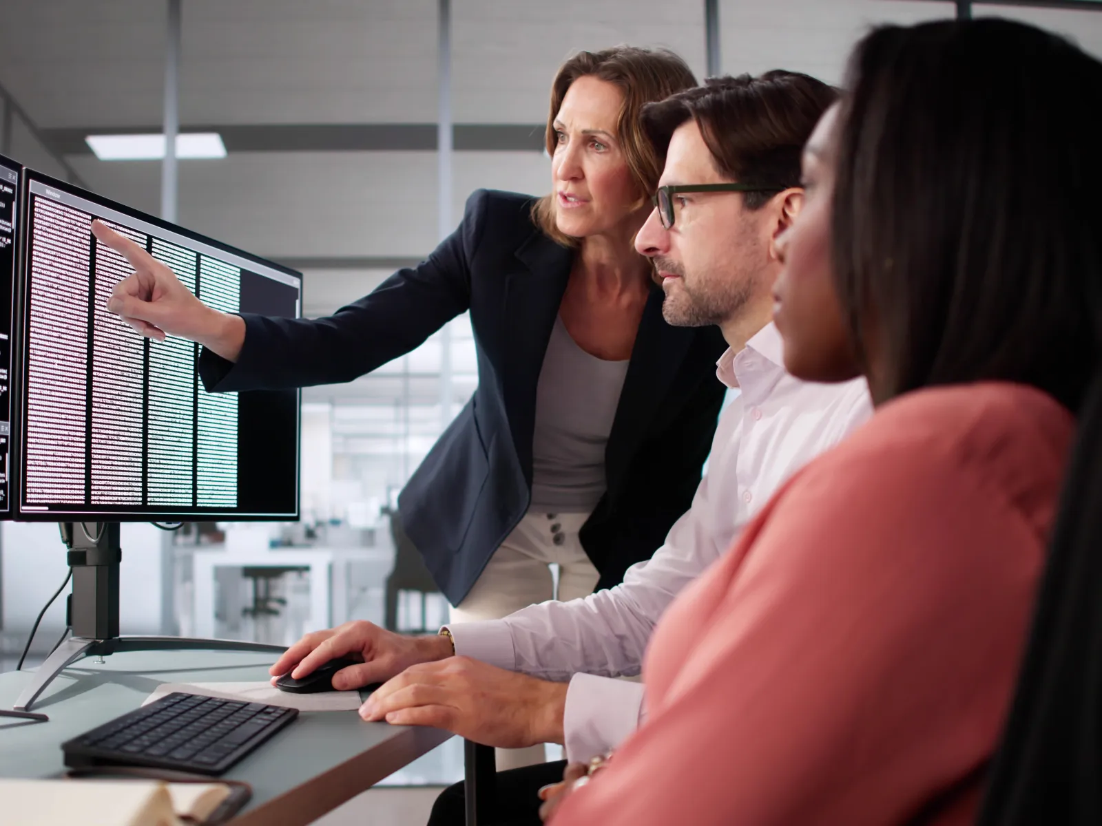 Team of software developers collaborating and reviewing code on multiple computer monitors in modern office.
