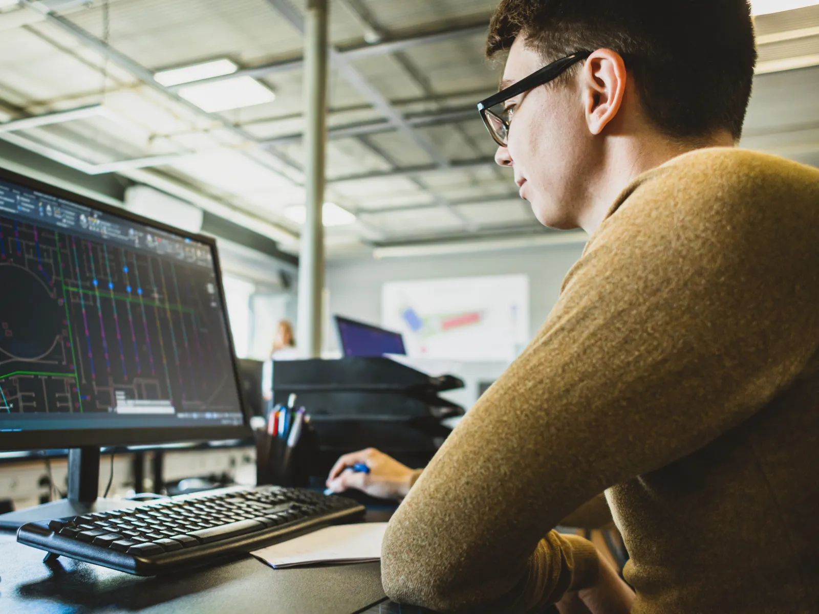 Young man working on computer with architectural or engineering design software in modern office workspace