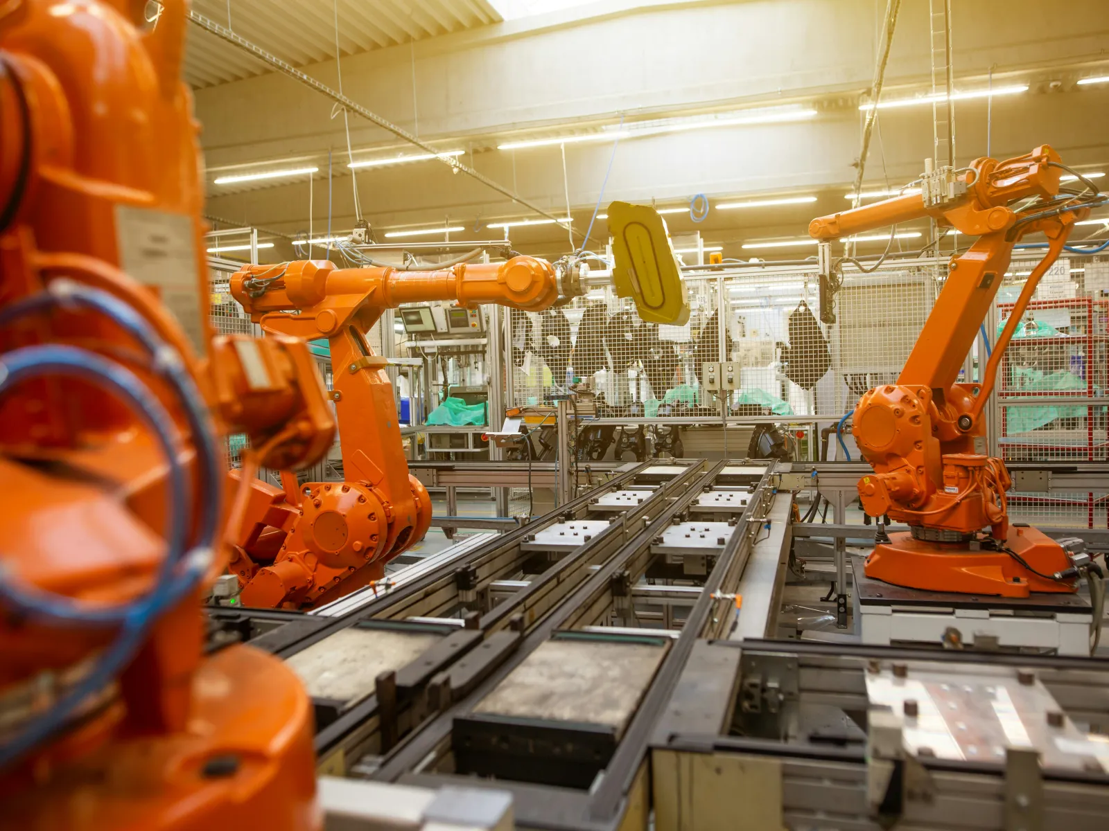 Orange robotic arms operating on automotive assembly line in a modern factory environment with bright lighting