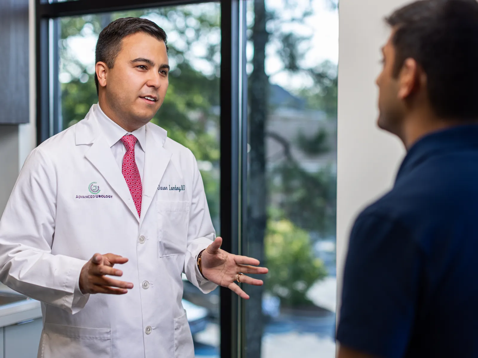 Male doctor in white coat explaining medical information to patient in a bright clinic room.