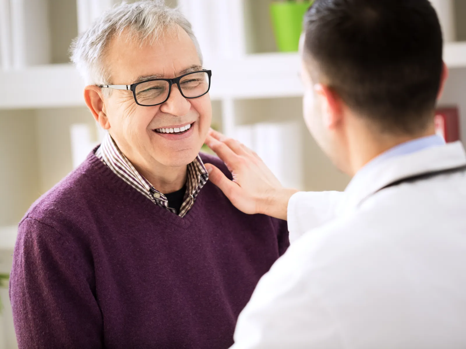 Smiling elderly man wearing glasses talks with doctor in white coat during medical consultation