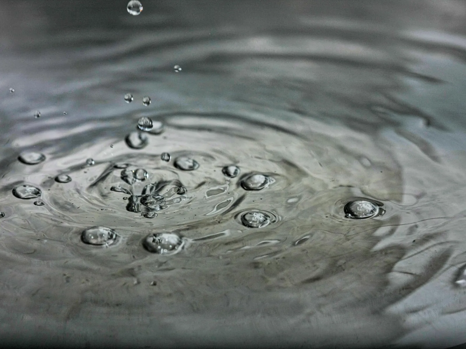 Close-up of water droplets creating ripples on a calm water surface with gray reflections.