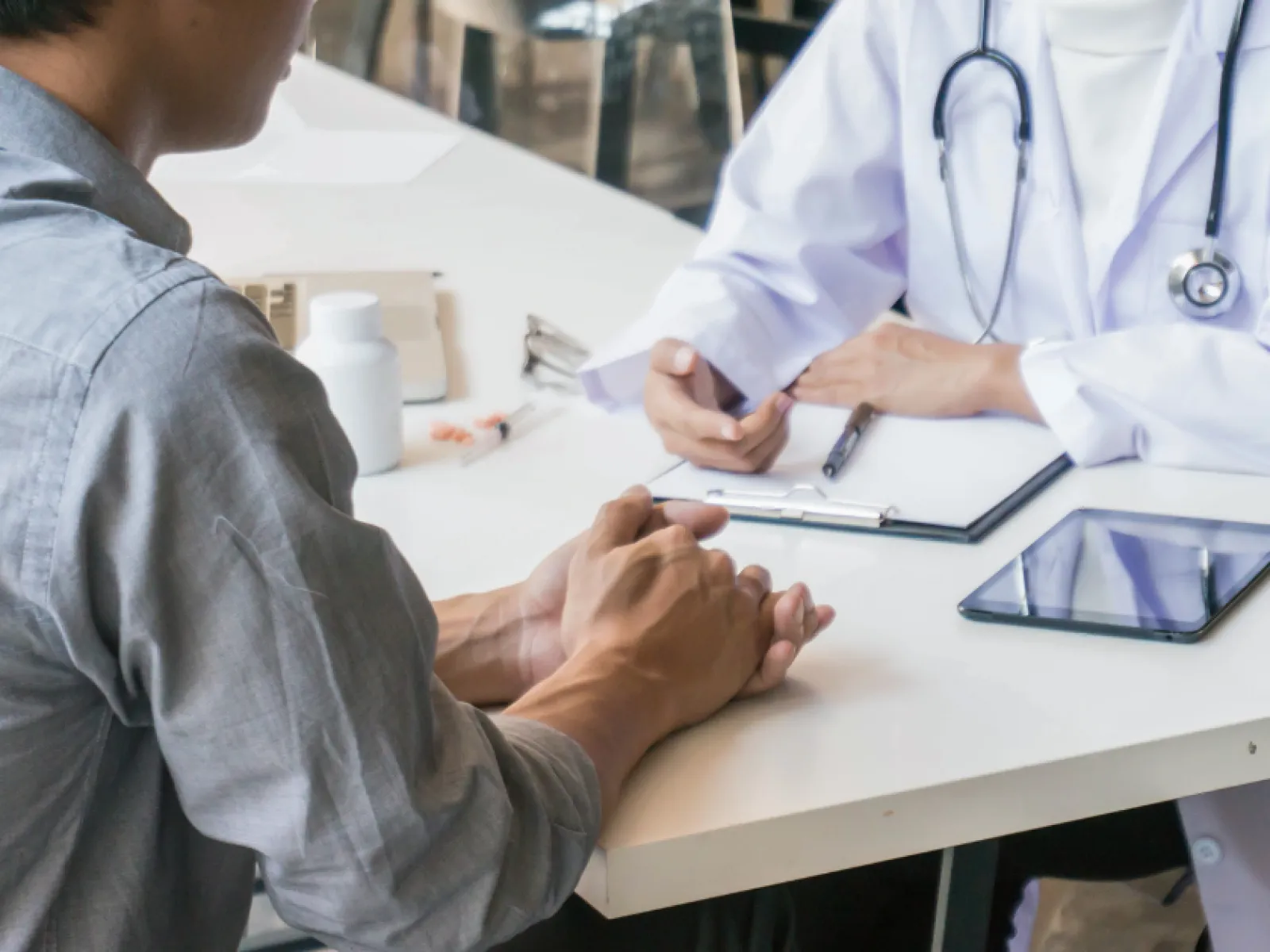 Patient consulting with a doctor at a desk with medical tools and prescription bottle visible.