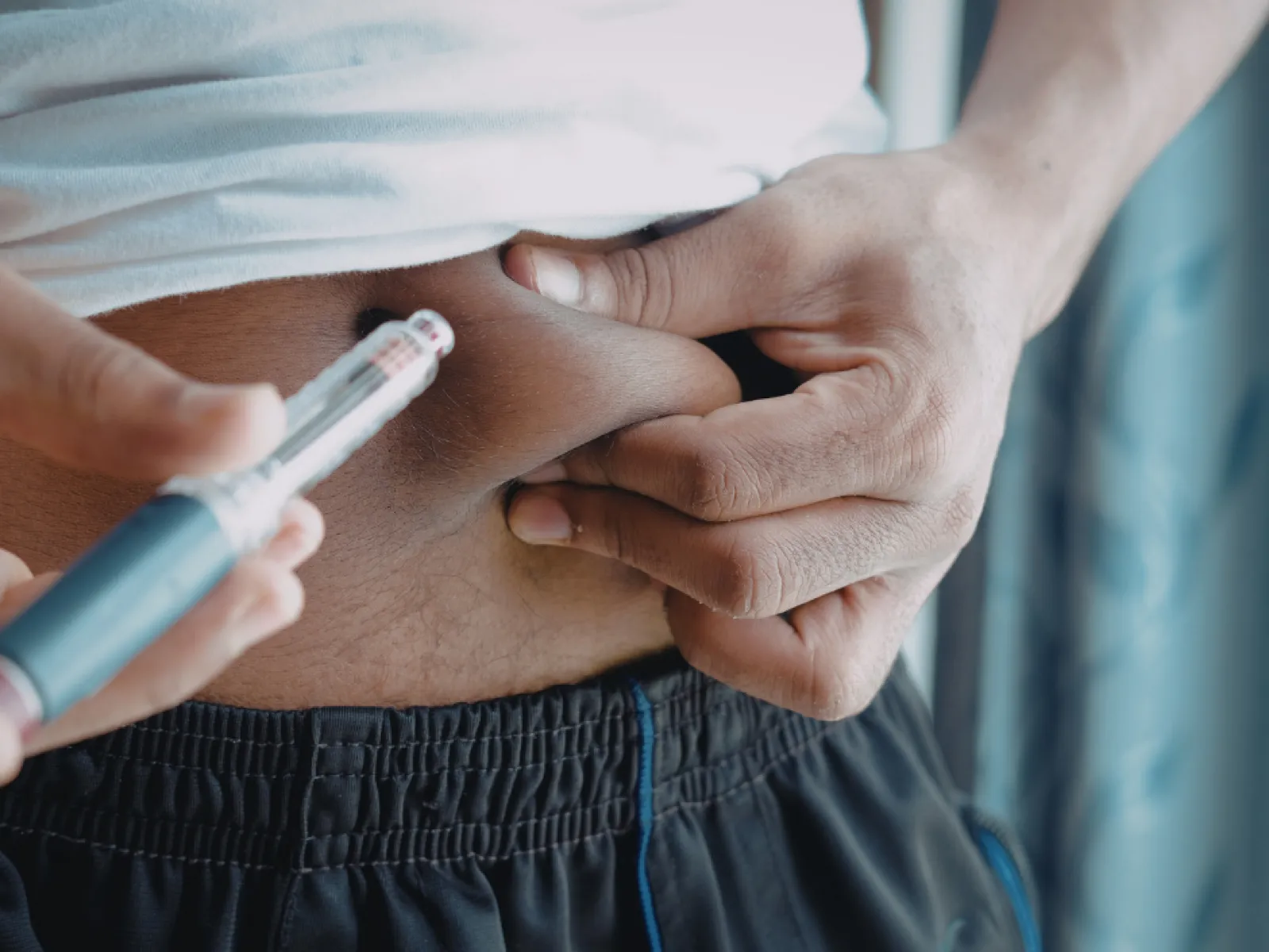 Person administering insulin injection into abdominal fat using insulin pen for diabetes management.