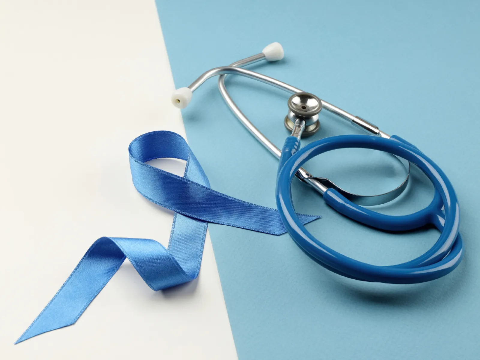 Blue prostate cancer awareness ribbon with a blue stethoscope on a split blue and white background.
