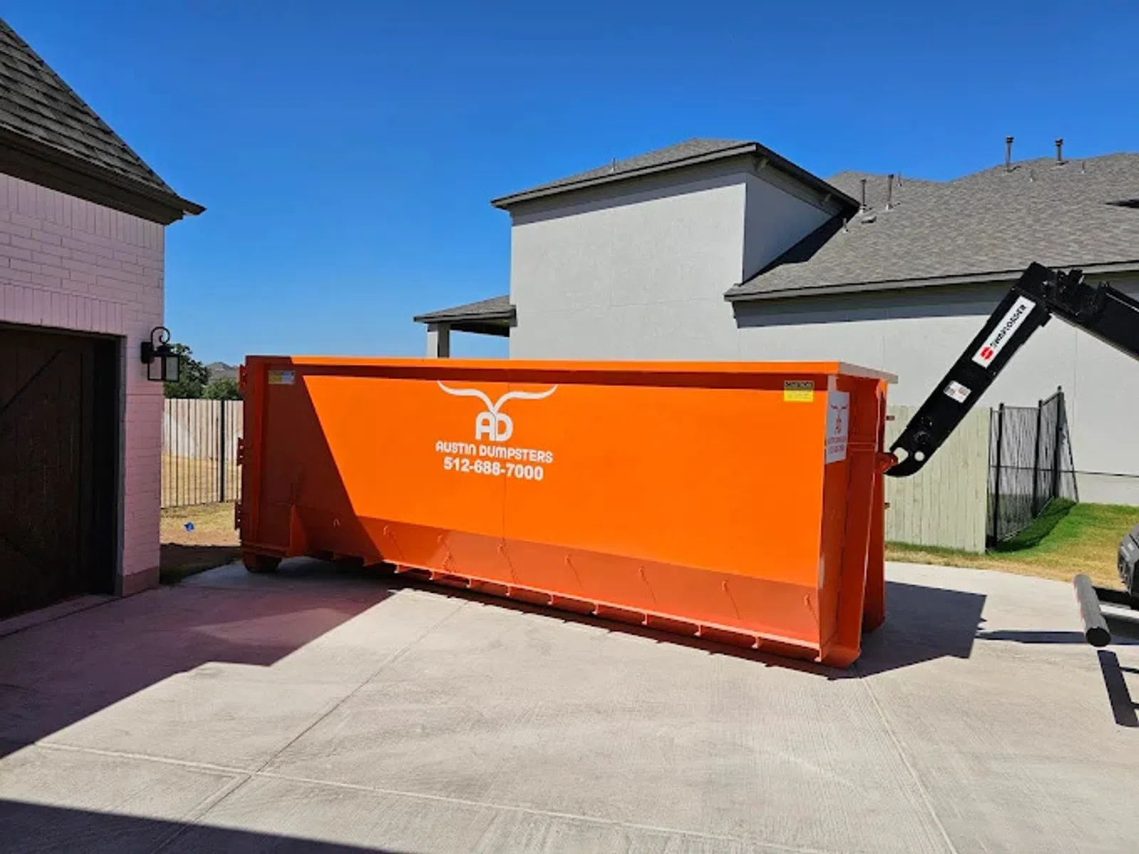 Large bright orange Austin Dumpsters container placed in a residential driveway on a sunny day.