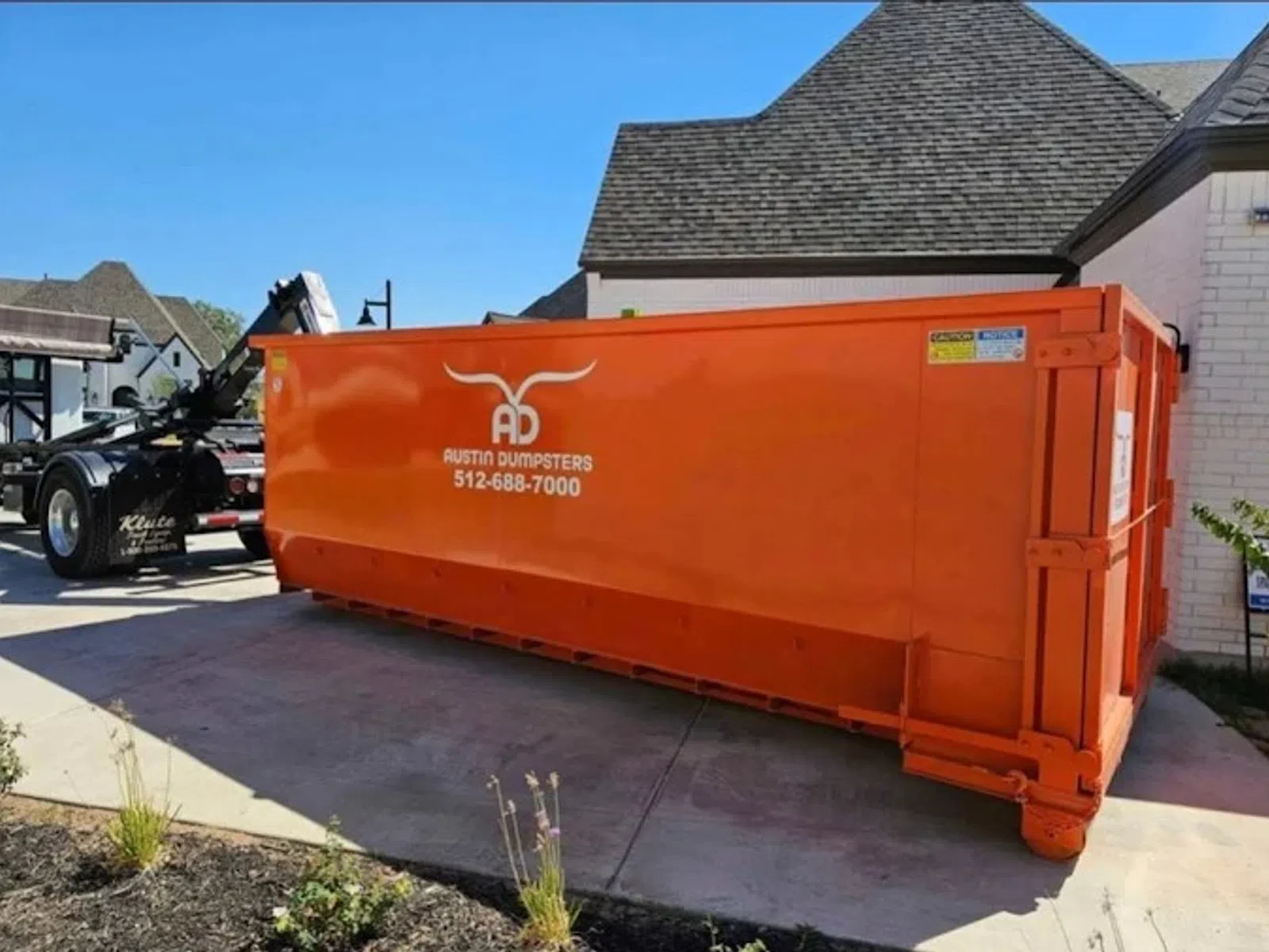 Large orange Austin Dumpsters container parked beside a residential driveway under clear blue sky