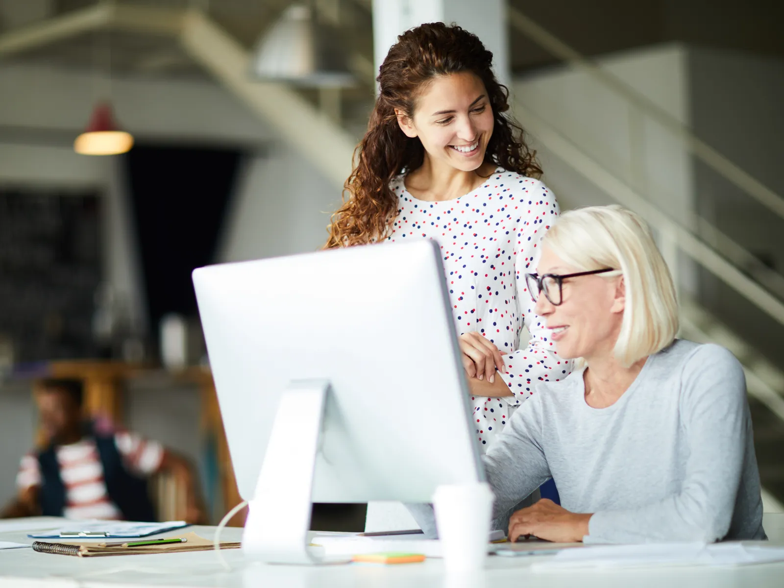 Two women collaborating happily at a computer in a modern bright office environment