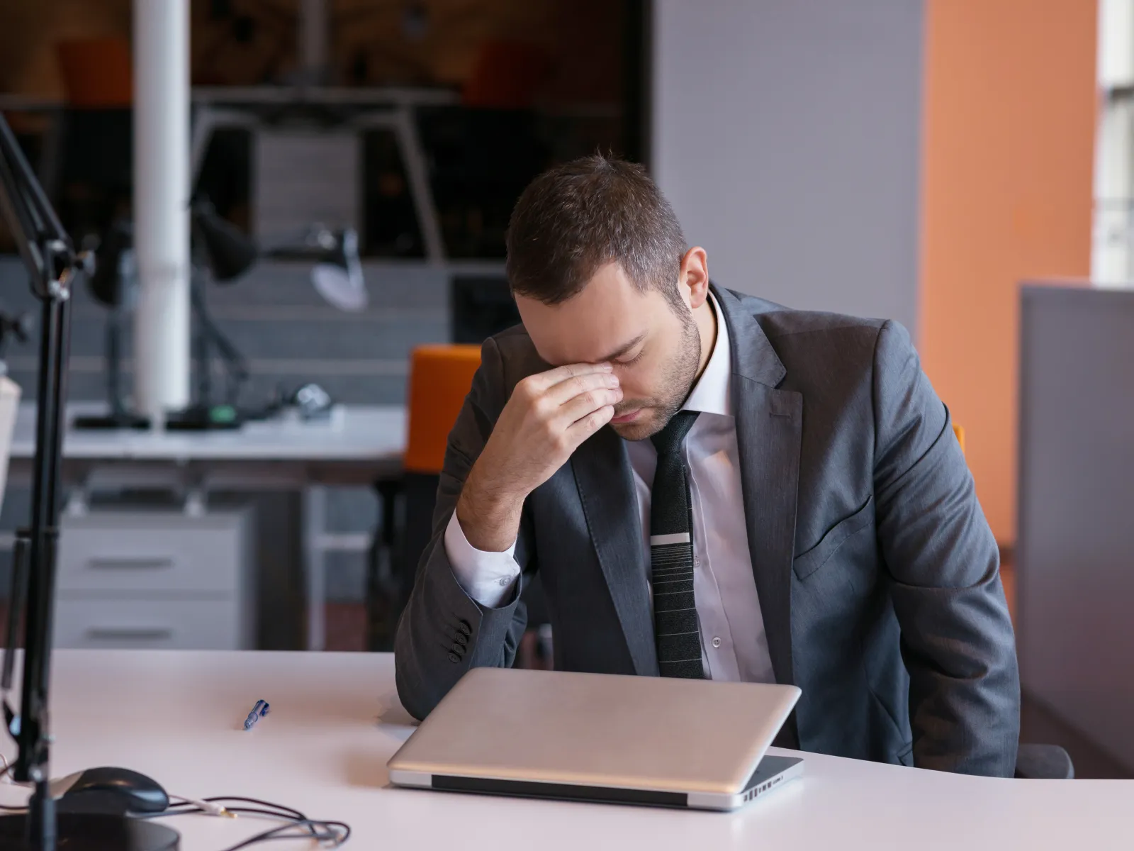 Man with glasses concentrating thoughtfully on laptop screen at home office desk with plant nearby