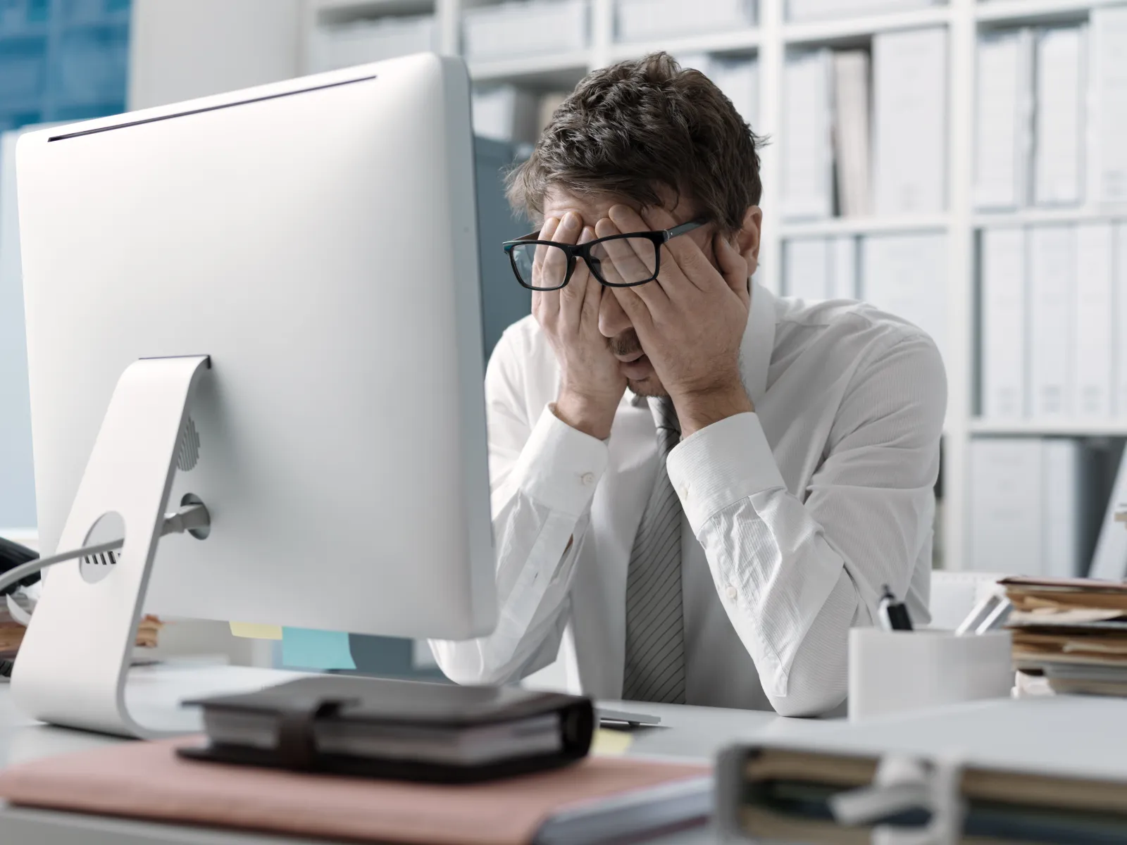 Stressed businessman sitting at desk in front of computer with hands covering his face in office.