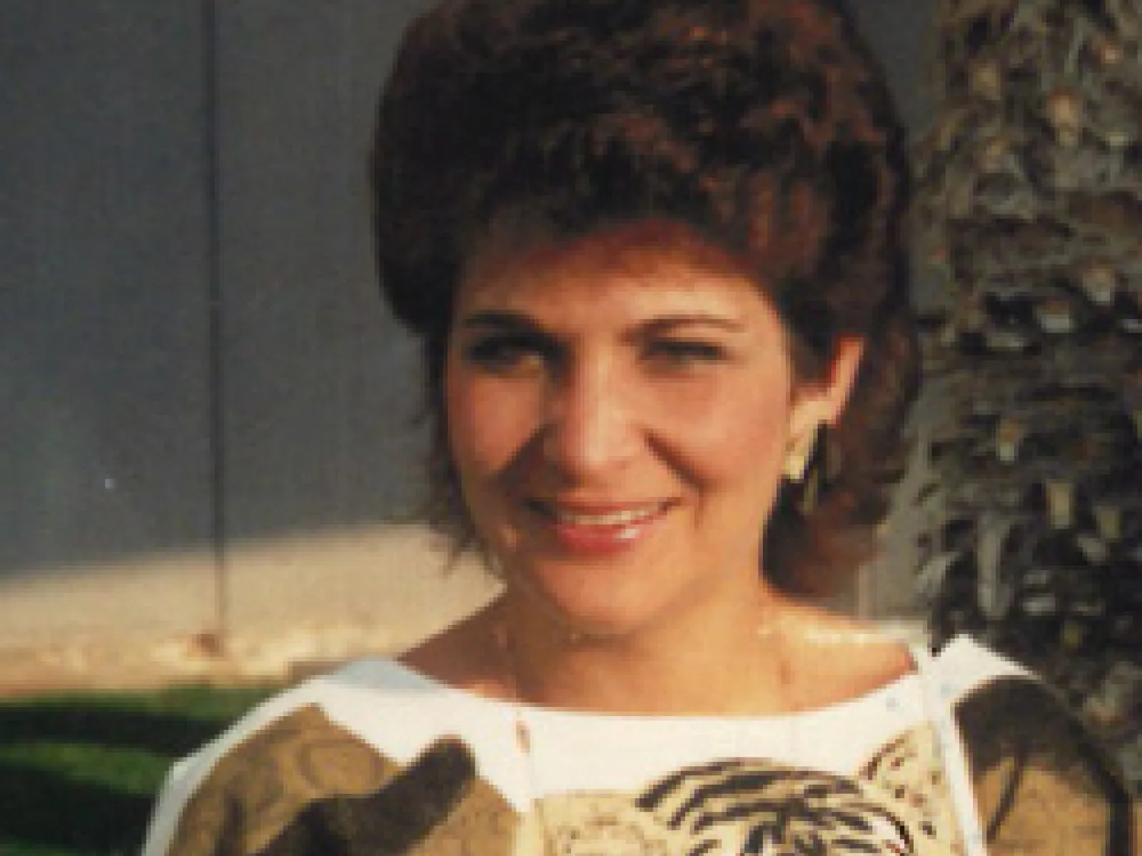 Smiling woman with short curly hair wearing a beige and white tiger print sweater outdoors on a sunny day