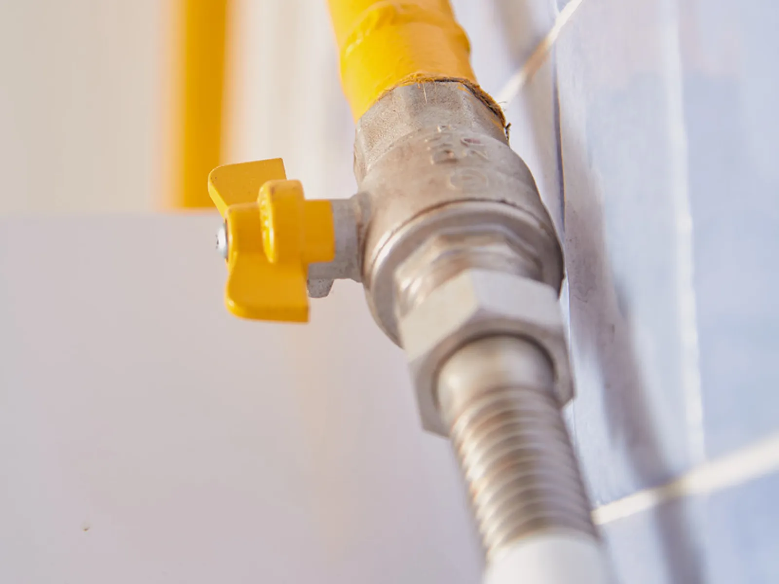 Close-up of a yellow gas pipe with a valve connected to tiled wall, highlighting plumbing details.