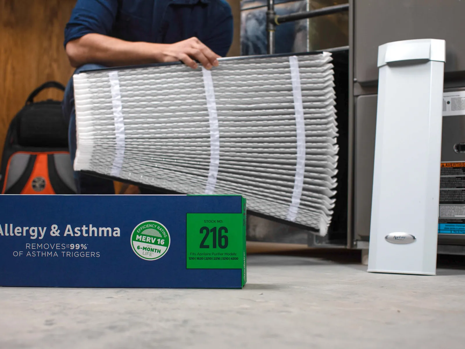 A person holding an air filter next to an air purifier and a box labeled for allergy and asthma relief.
