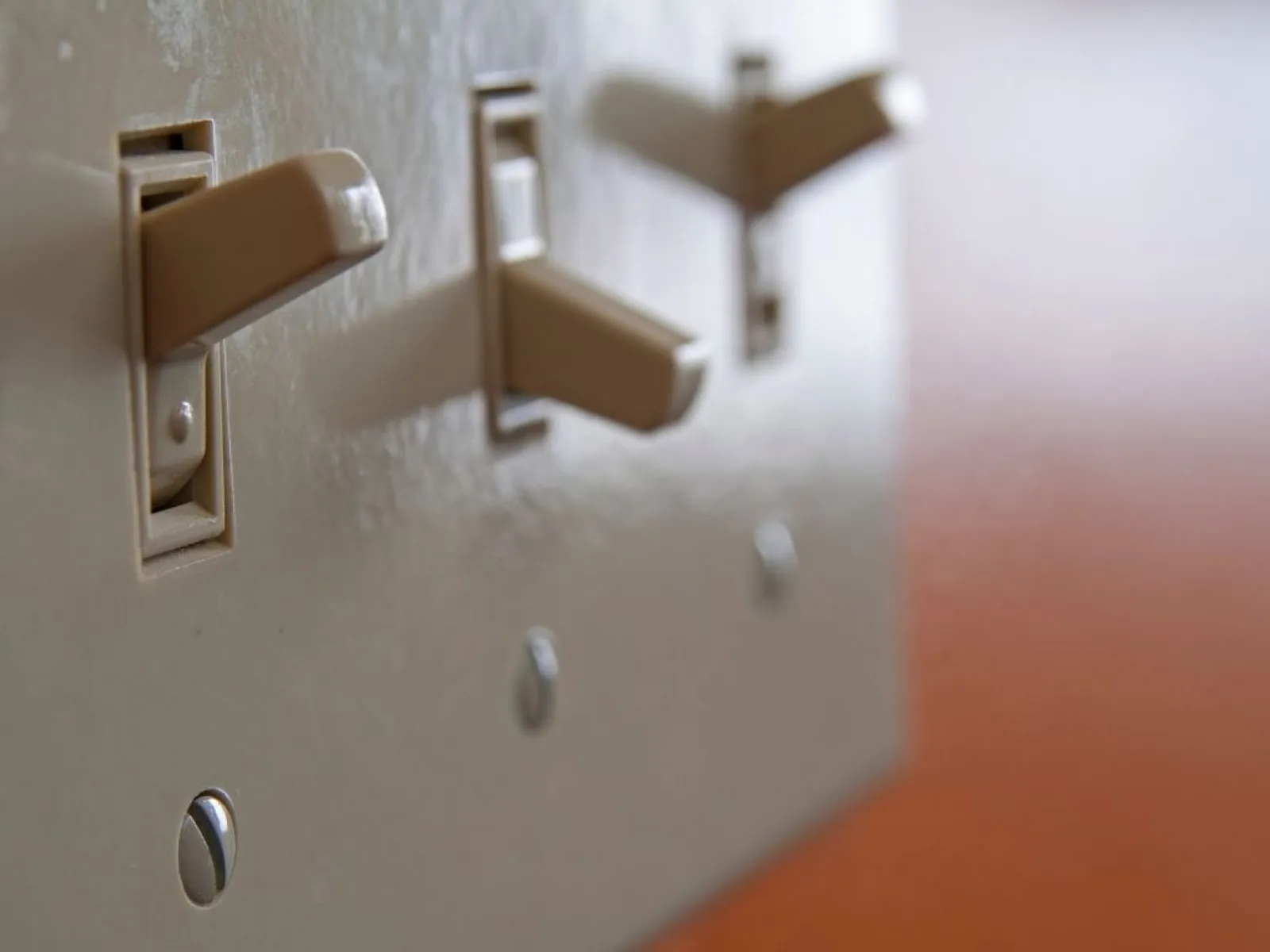Close-up of three beige light switches on a wall with one switch in the on position and two off.
