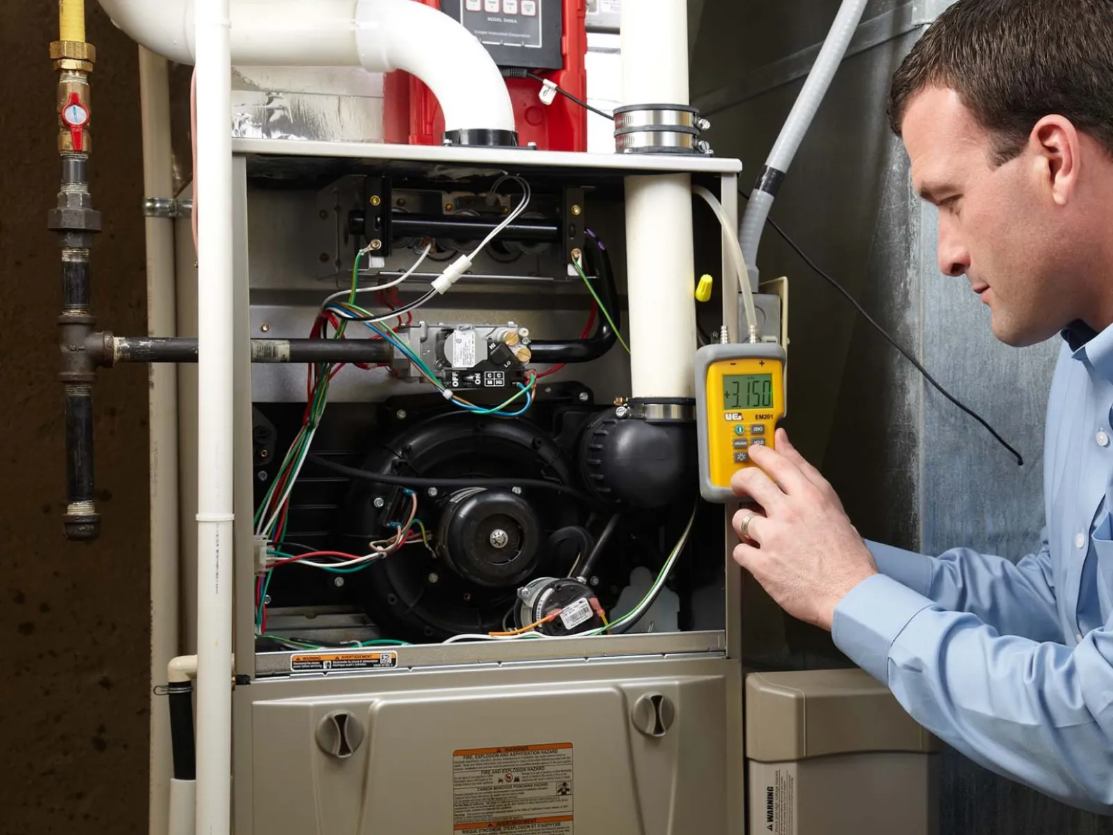 Technician checking a furnace's electrical components with a multimeter for maintenance.