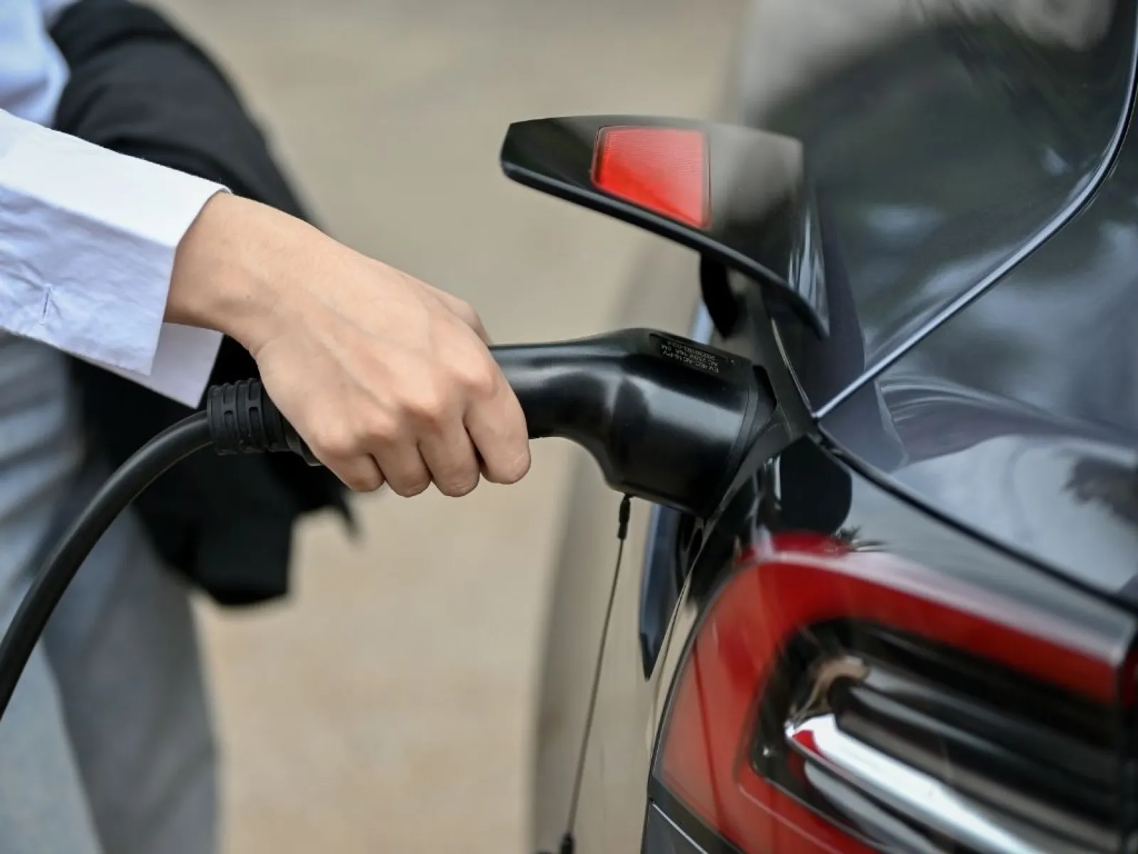 Person plugging in an electric car charger into a black electric vehicle at a charging station.