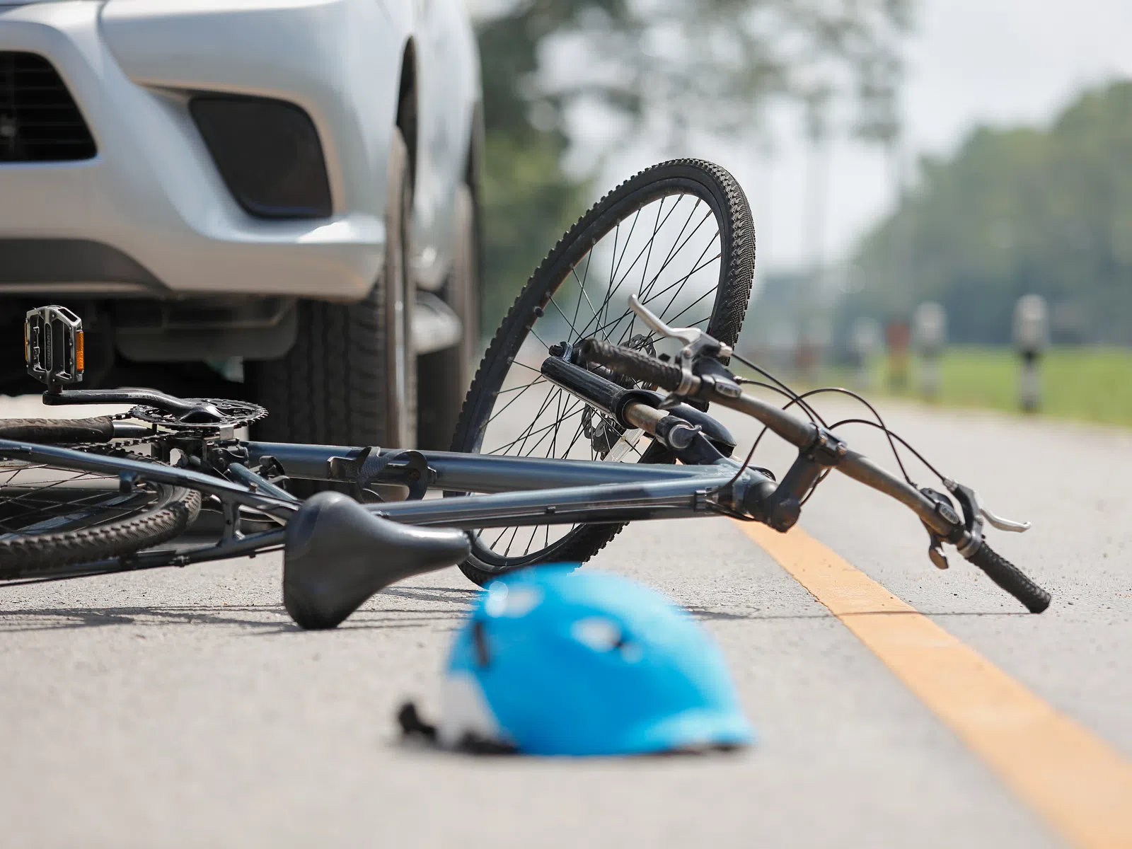 Bicycle and blue helmet lying on the road next to a white vehicle indicating a possible accident.