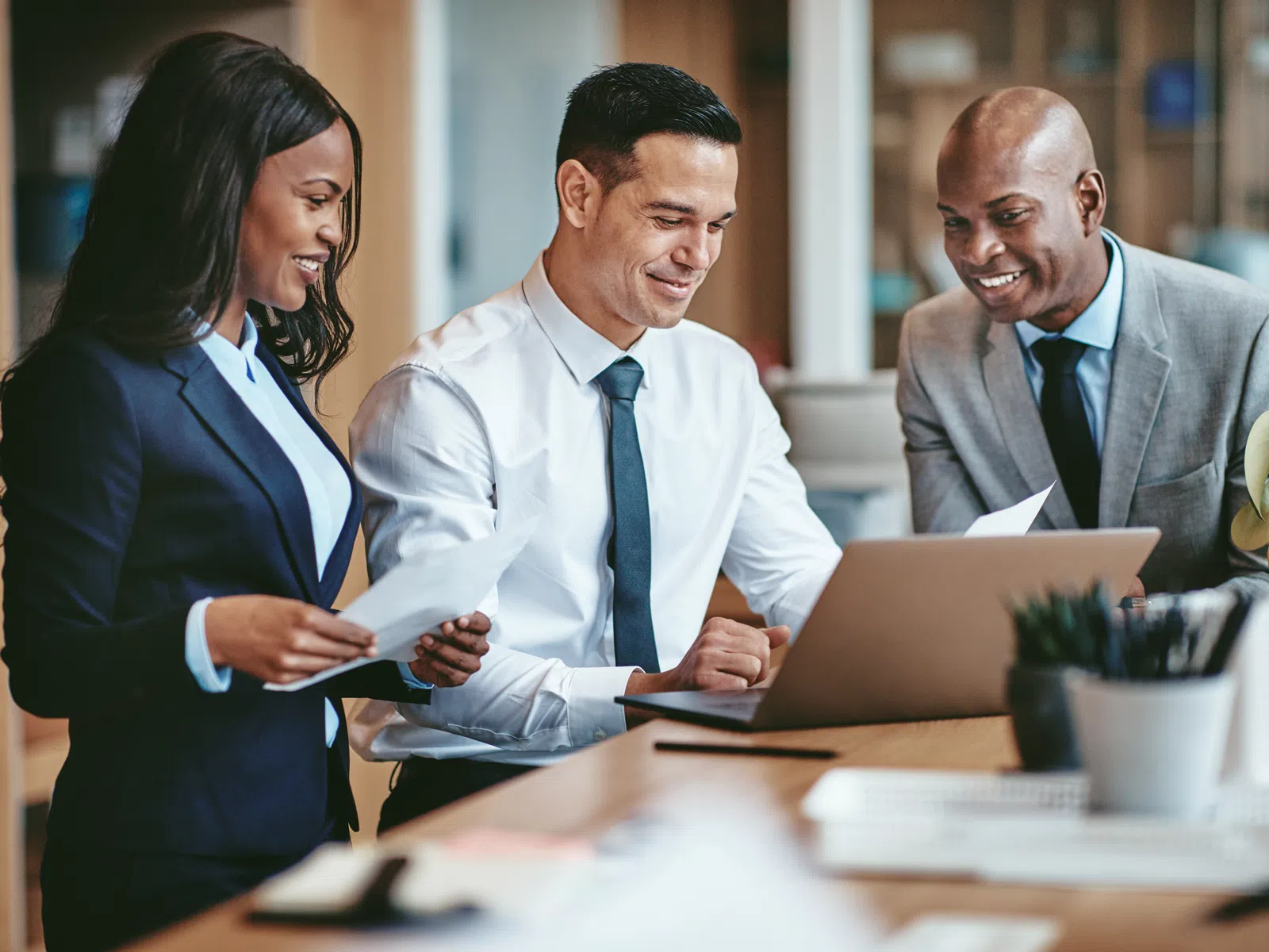 Three diverse business professionals discussing documents and working together at a laptop in a modern office.