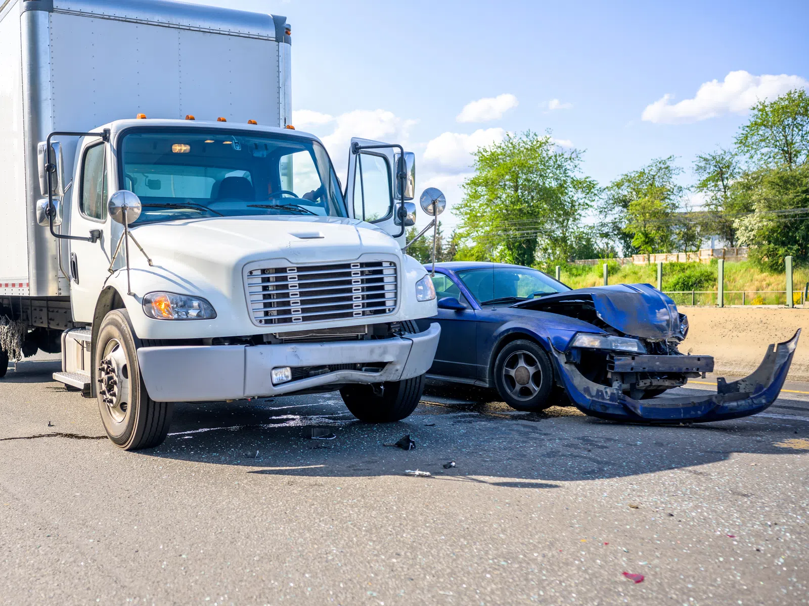 White delivery truck and blue car involved in collision on sunny road with visible damage to car front.